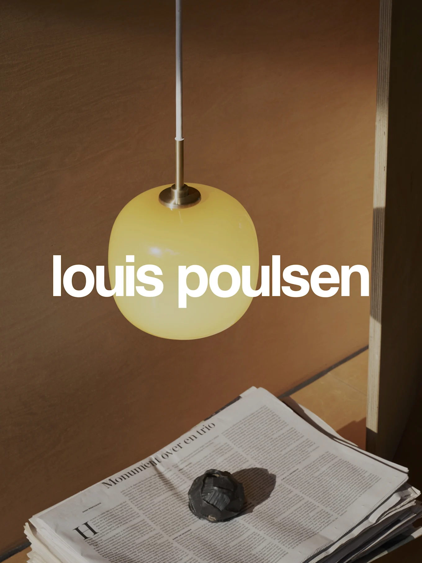 Louis Poulsen-logo over een warme scène met een gele bolvormige hanglamp, gestapelde kranten en een donker decoratief object.