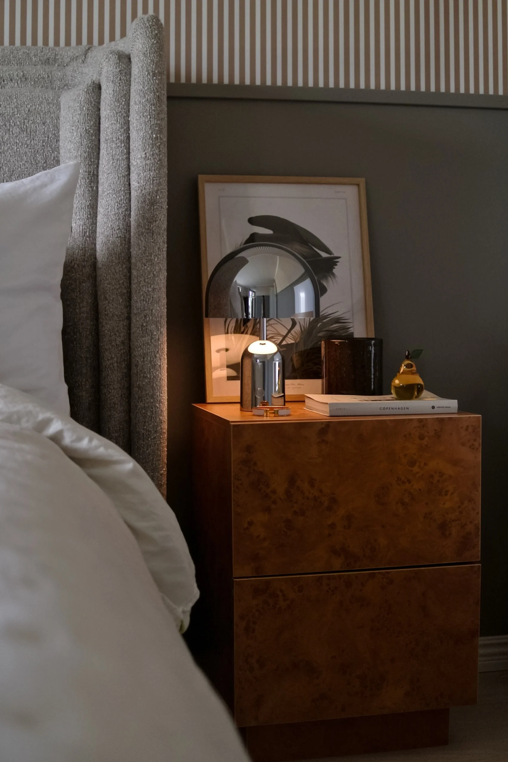 Een moderne eetkamer met een tafel gedekt met witte borden, heldere glazen, een vaas met witte lelies en een hoge kaars, alles onder een zwarte, meerlaagse kroonluchter met zichtbare gloeilampen.
