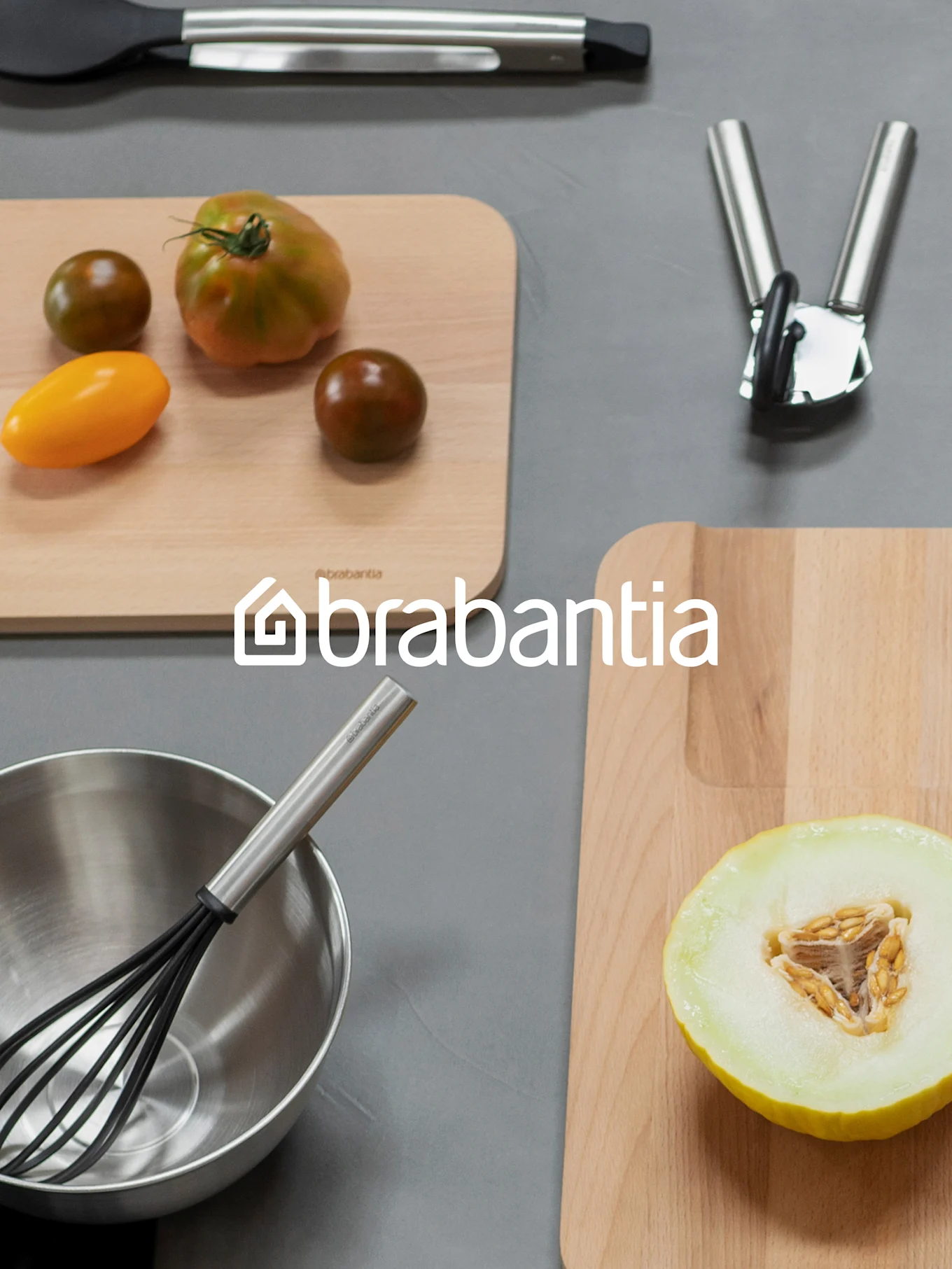 Brabantia-logo over een bovenaanzicht van keukenartikelen, waaronder snijplanken met tomaten en meloen, een garde in een kom en ander keukengerei.