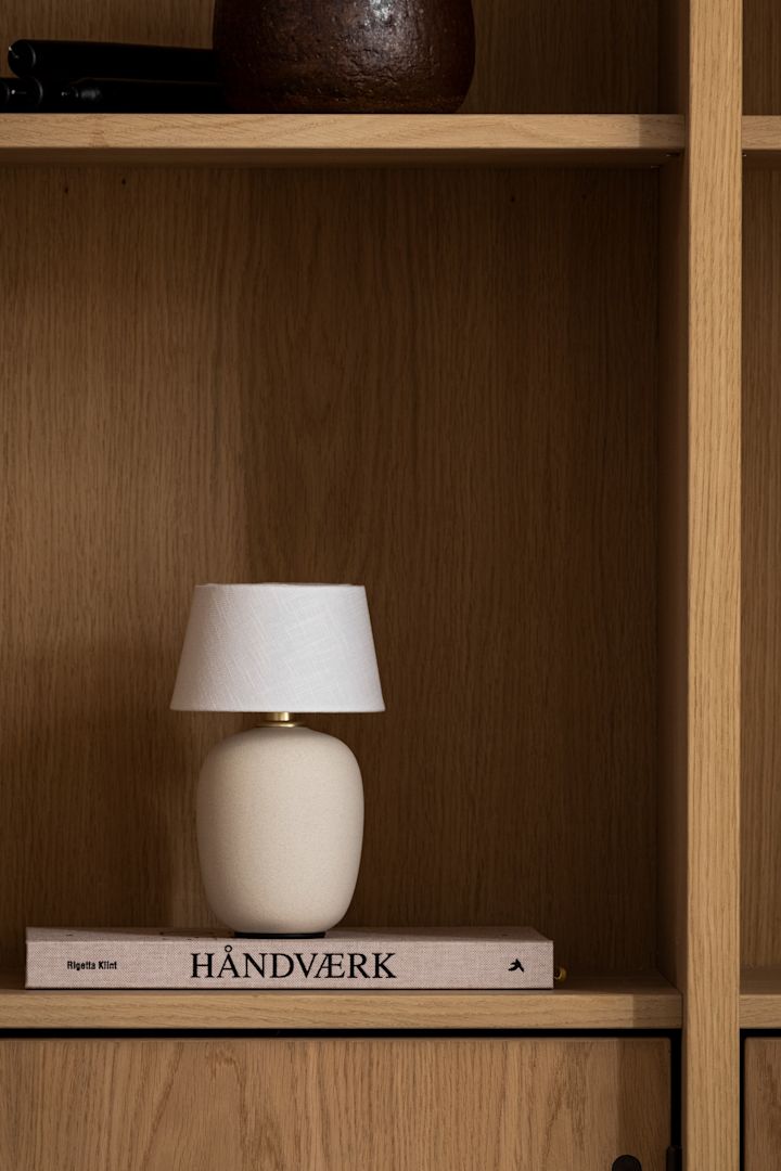 Ontdek de trend van de paddenstoellamp: Hier zie je de draagbare Torso tafellamp van Audo Copenhagen in een houten boekenkast.