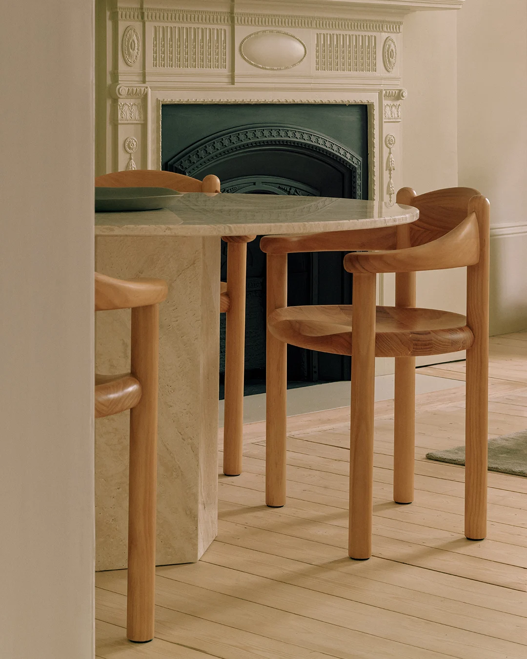 Een ronde marmeren tafel met twee lichte houten stoelen, voor een decoratieve open haard.