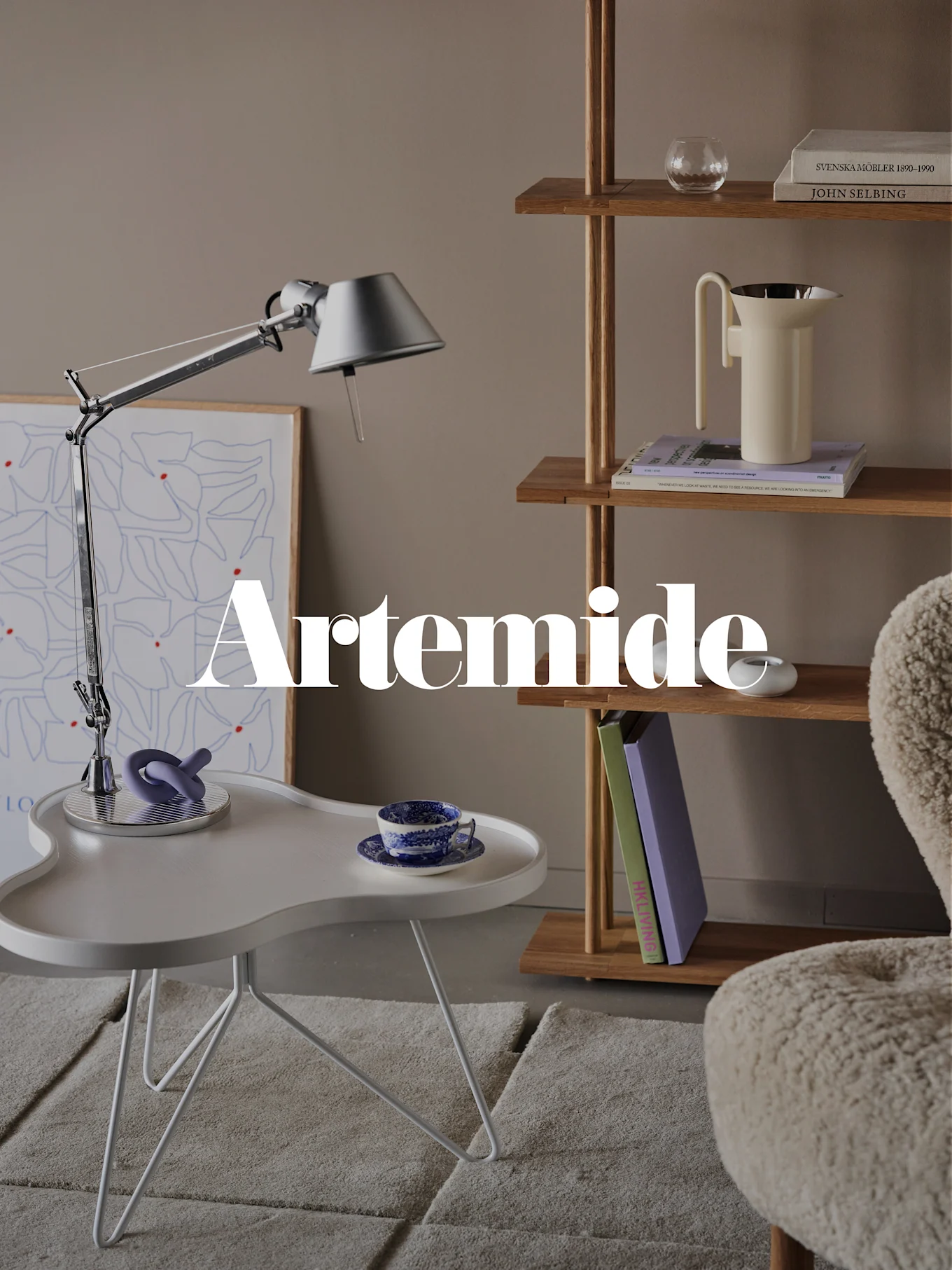 Een moderne woonkamer met een zilveren bureaulamp, witte bijzettafel, houten boekenkast en crèmekleurige fauteuil. Tekstoverlay: 'Artemide'.