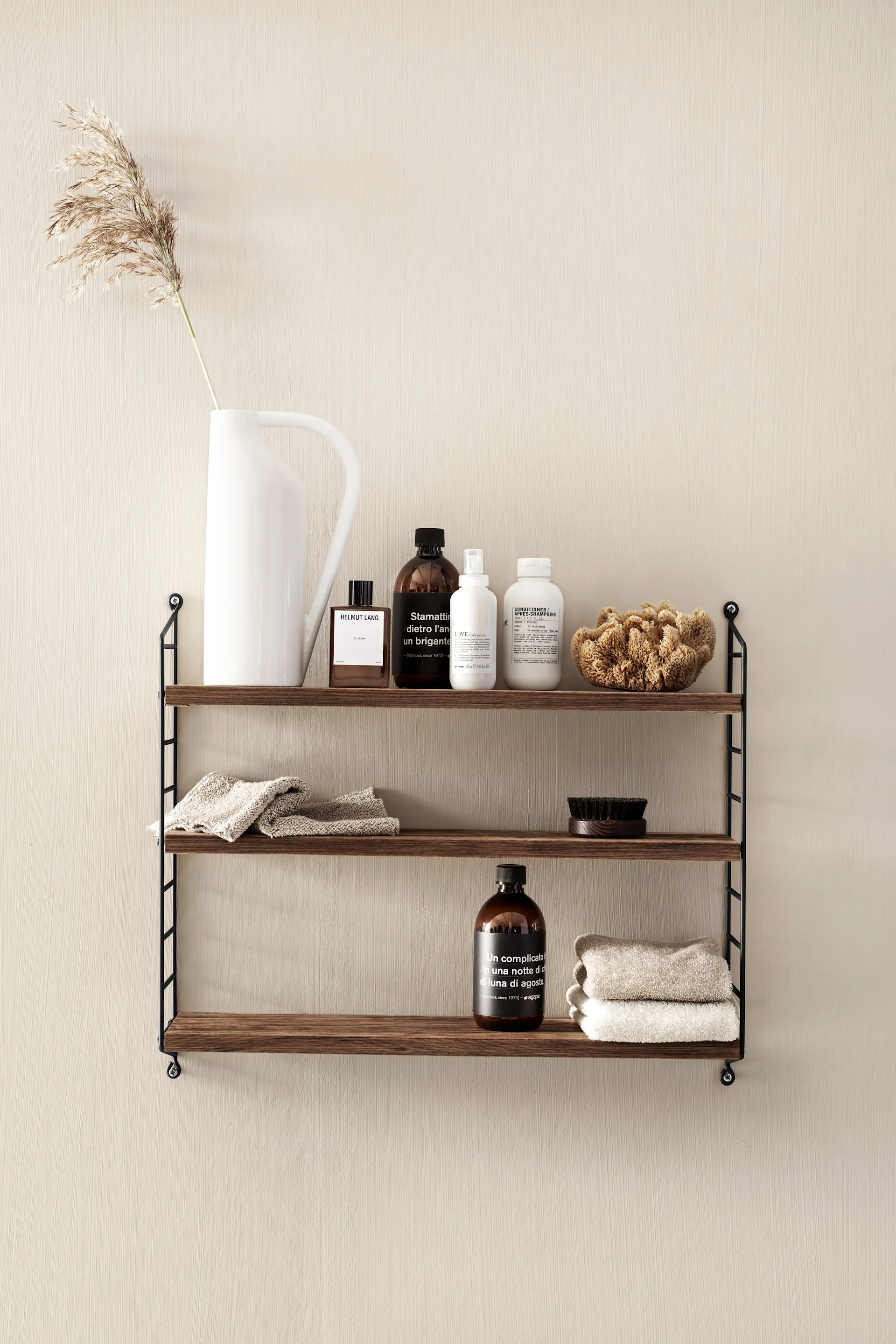 De foto toont de String Pocket in walnoot en zwart in een badkameromgeving. De String plank is geschikt voor alle kamers in huis en kan alles opbergen, van boeken tot gadgets.