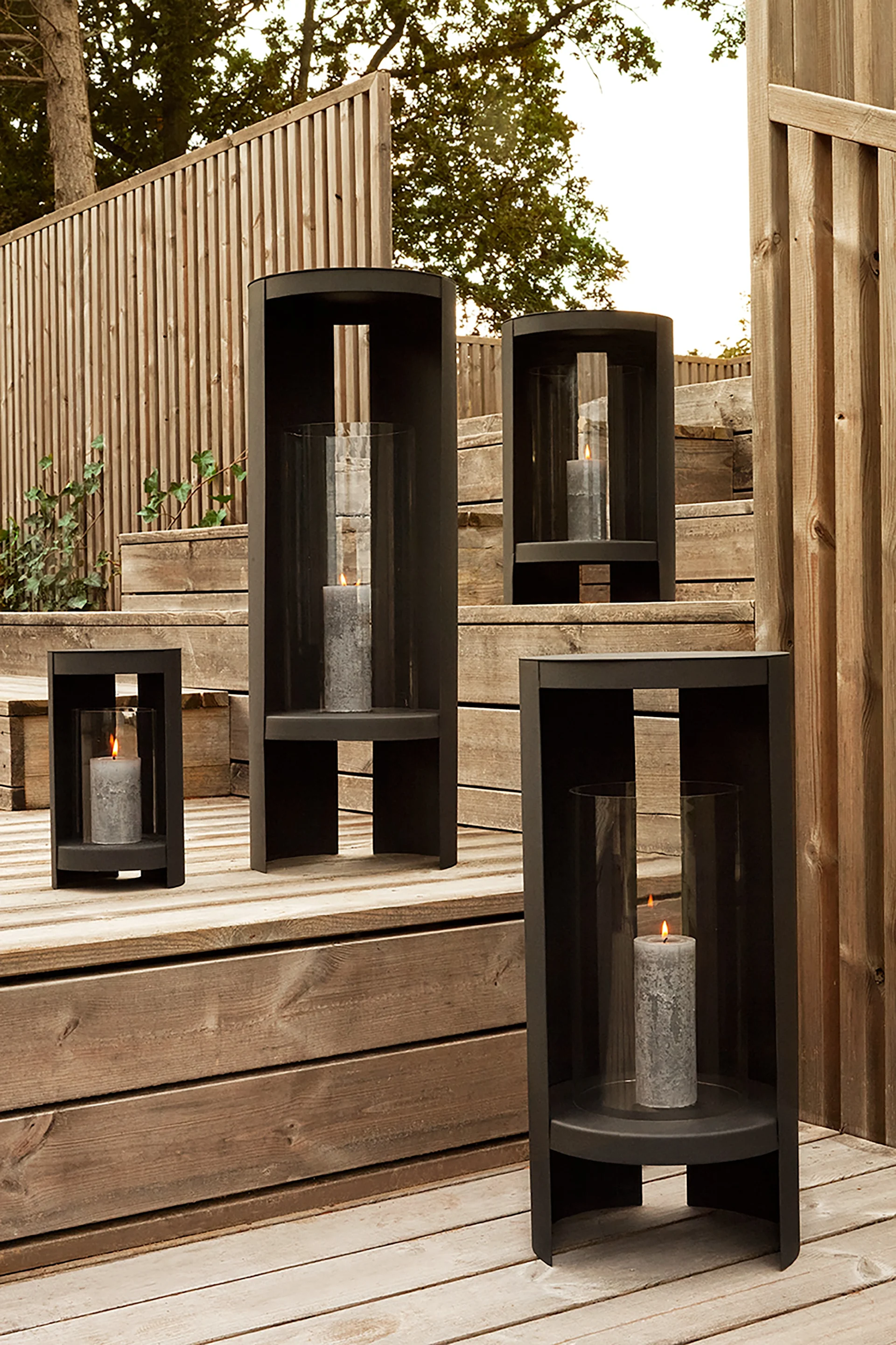 Lantaarns en windlichten voor buiten - hier zie je de Oro lantaarn van AYTM in zwart en in verschillende maten op een houten trap in een tuin staan.