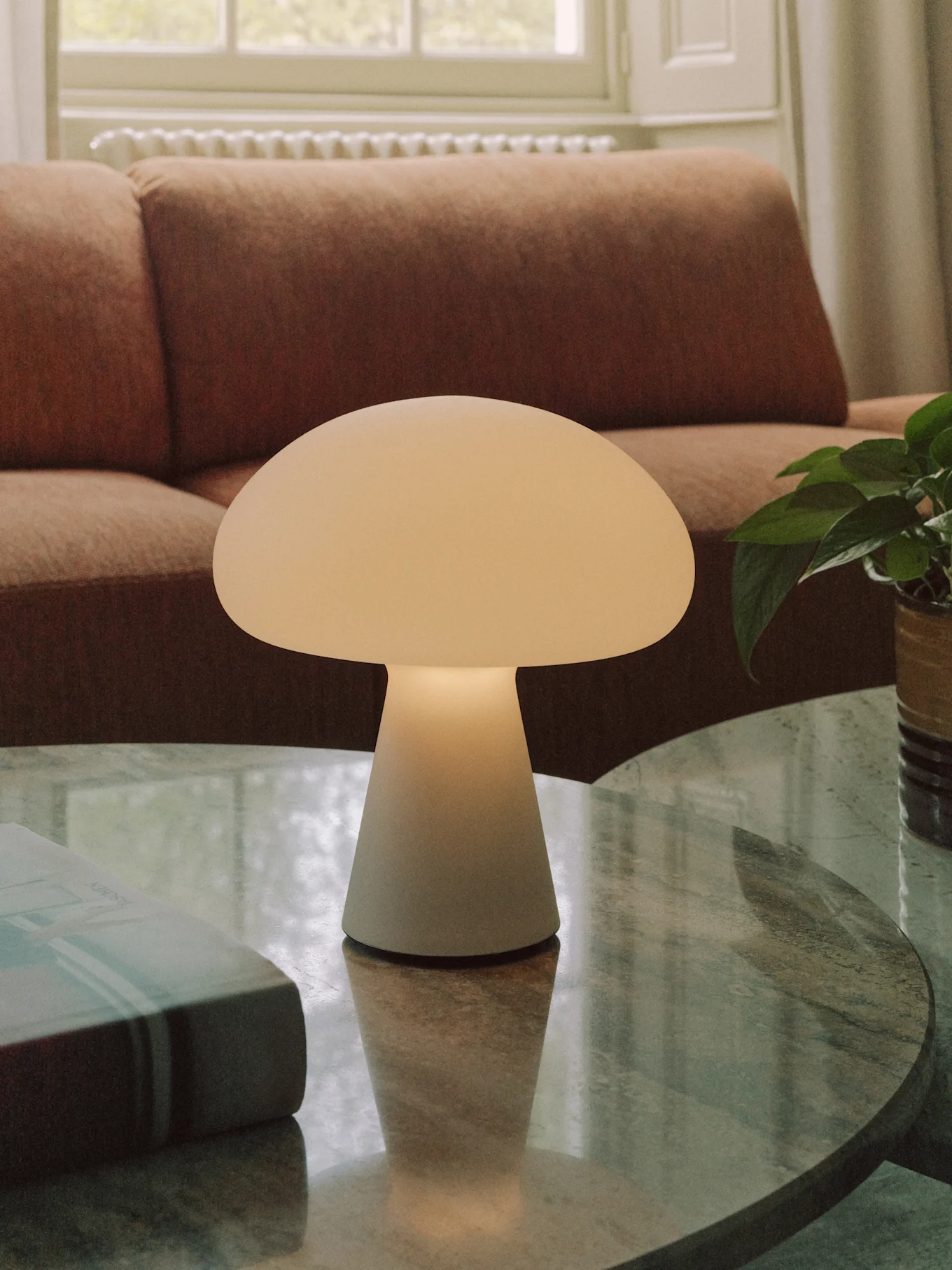 Een gebroken witte paddestoelvormige tafellamp staat op een ronde marmeren salontafel in een woonkamer.