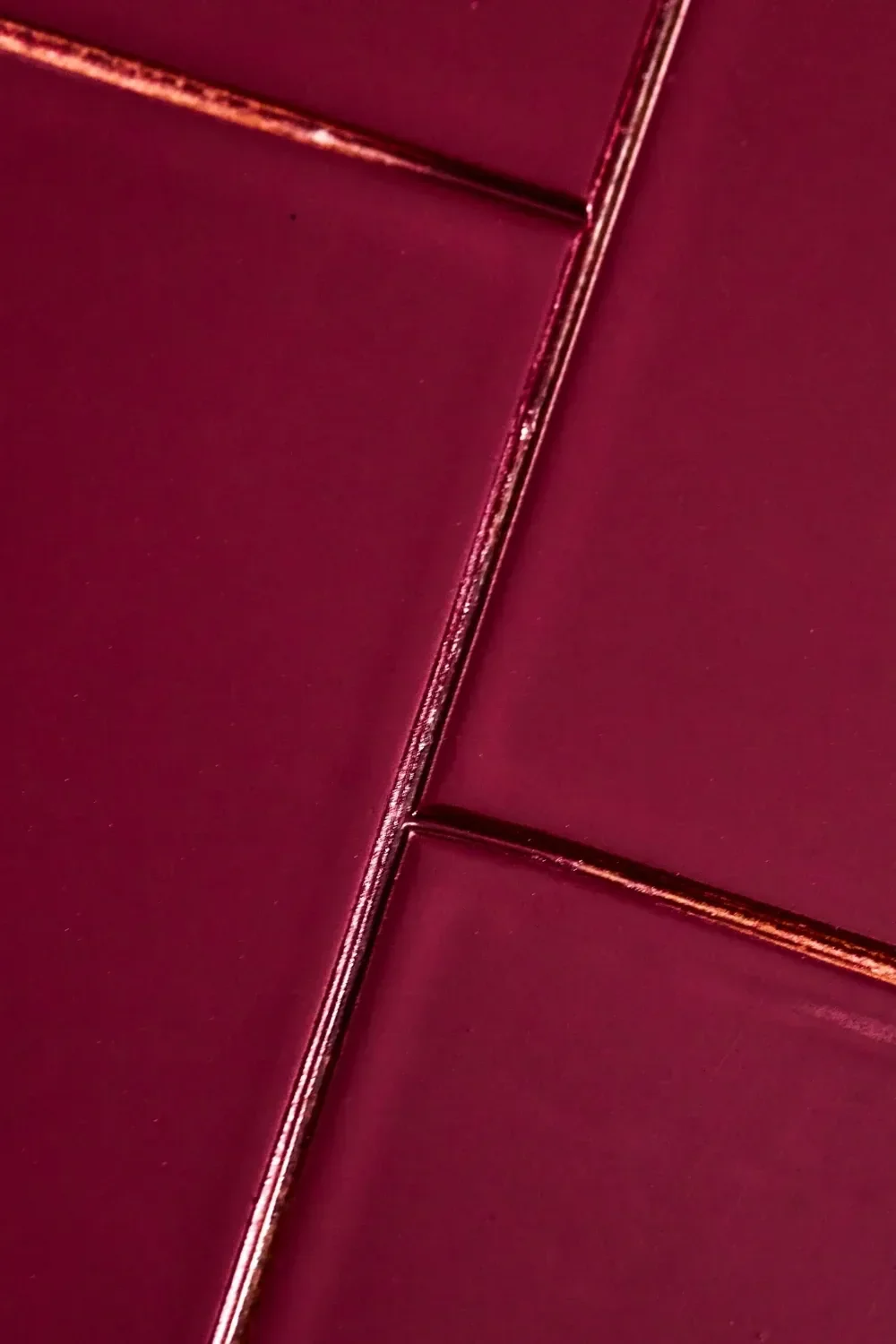Glanzende donkerrode tegels met metallic roodbruine voegen.