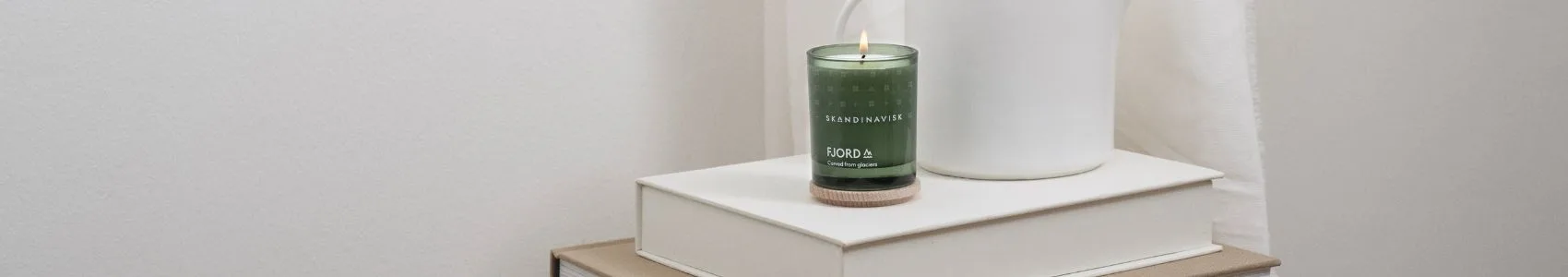 Een boek met de titel 'NOTES FROM THE FELLS' op een grijze deken naast twee Scandinavische kaarsen, één zwarte brandend, één bruine met een houten deksel.