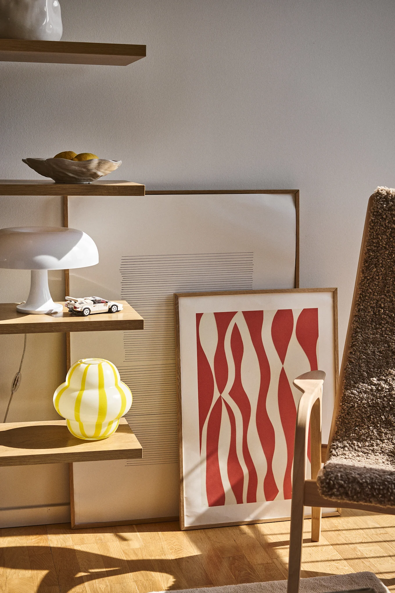 De Curlie-vaas van Byon heeft een ronde, bolvormige ontwerp in geel- en wit gestreept glas. Hier staat deze in een open boekenplank, samen met een Shell-schaal, lampen en schilderijen.