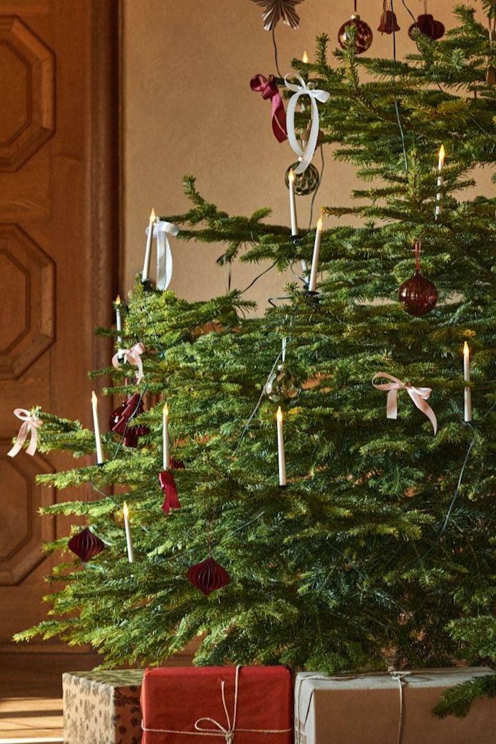 Traditionele kerstboomdecoratie-ideeën omvatten dingen zoals de elektrische boomkaarsen en strikken die je hier ziet op een boom met rode, witte en gouden decoraties. 