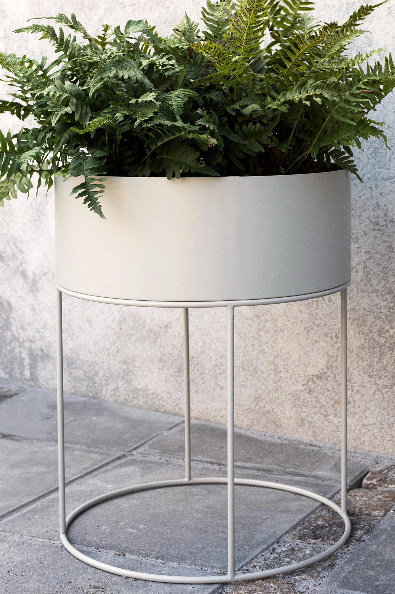 Bloempotten voor buiten: De grote ronde metalen plantenbak van Ferm Living met een grote groene varen staat op een terras.