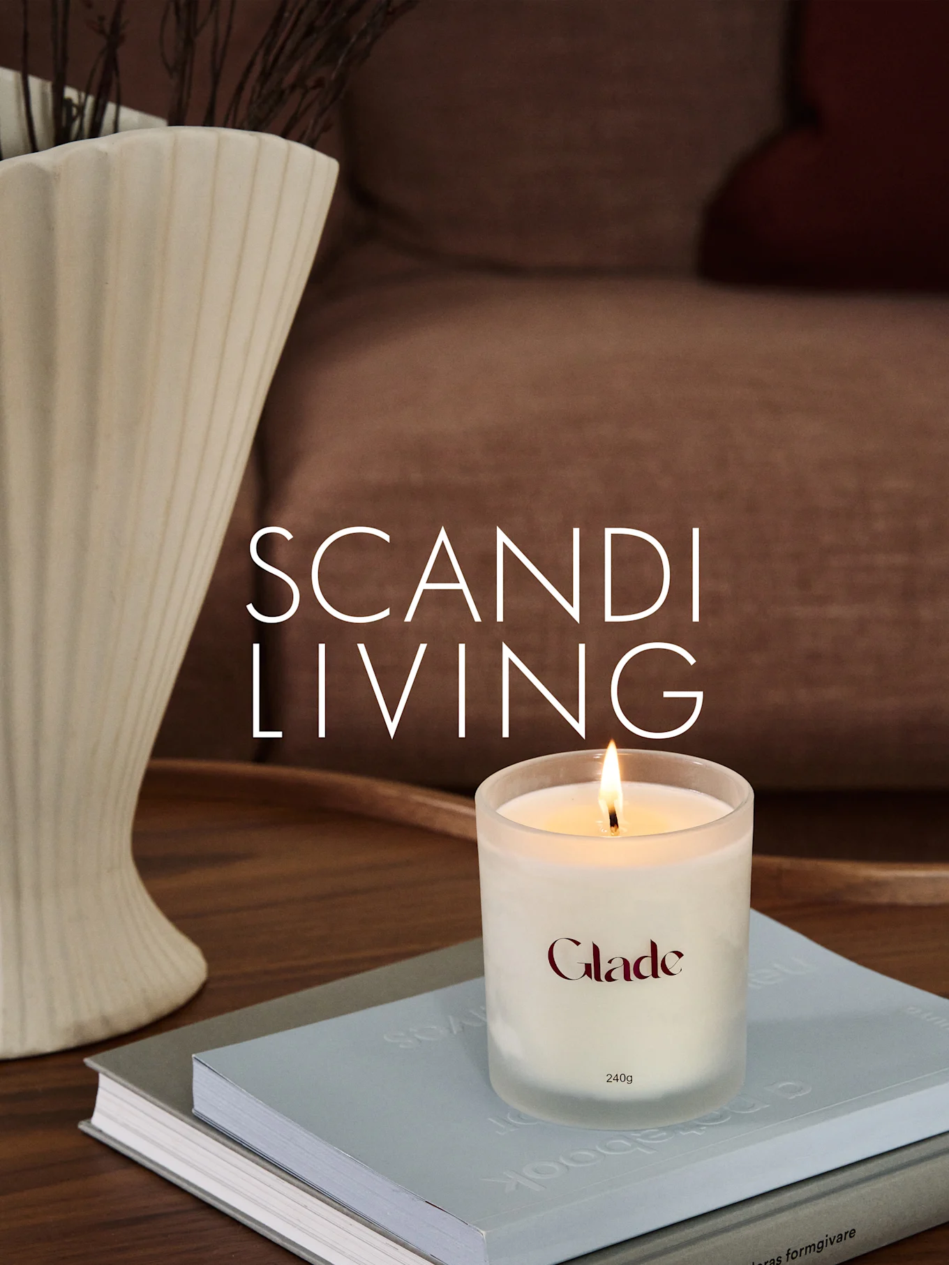 Een brandende Glade-kaars op boeken, naast een geribbelde vaas met takken. Overlaytekst: SCANDI LIVING.