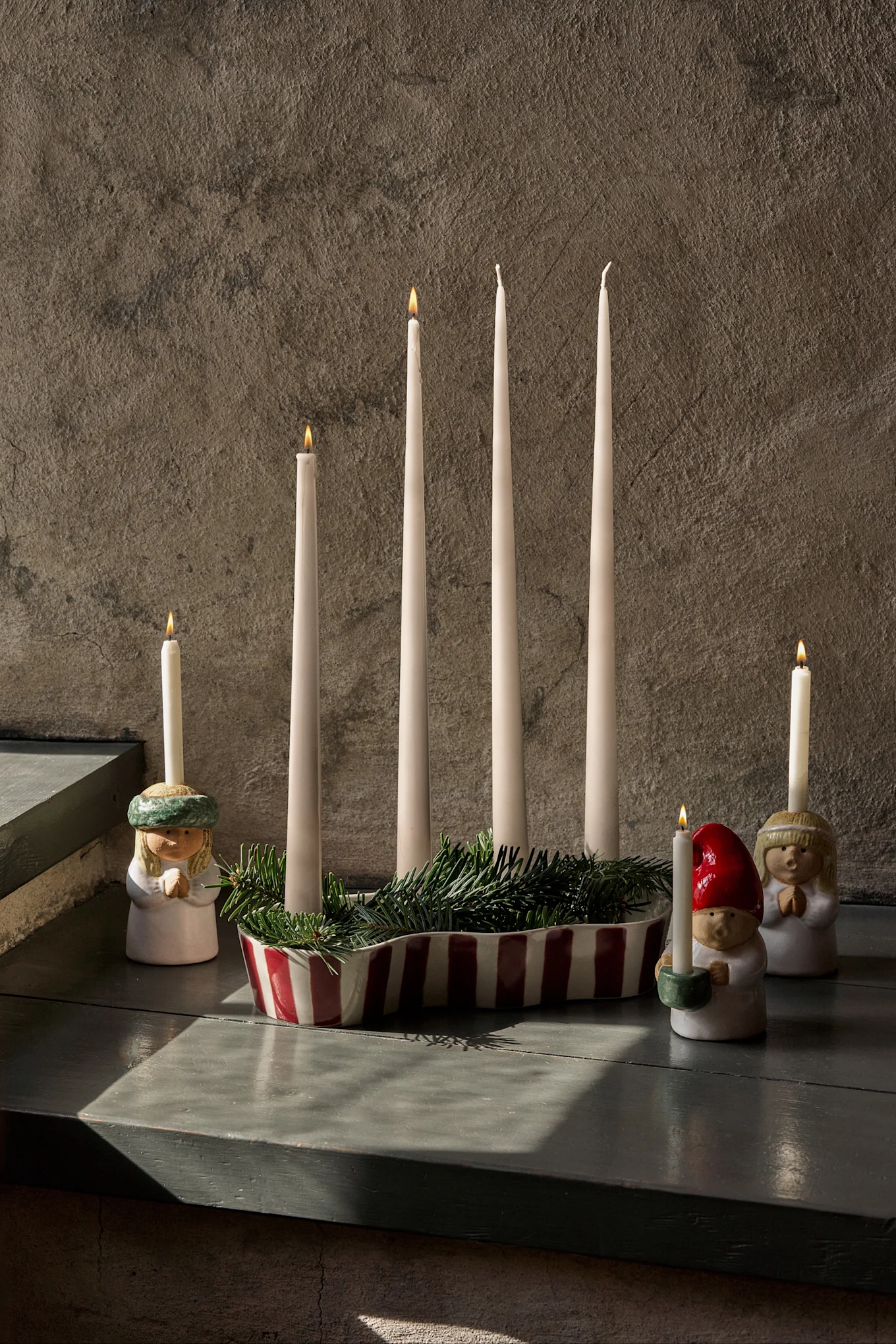 Adventsdecoratie met vier onverlichte kaarsen, groen dennenhout en drie beeldjes met brandende kaarsen.