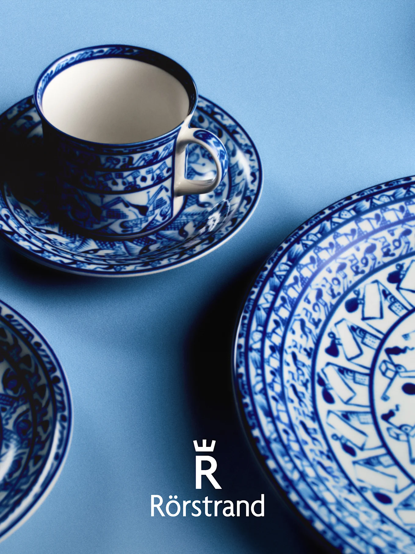 Blauw-wit gedessineerde theekop, schotel en bord op een lichtblauwe achtergrond, met Rörstrand-logo.