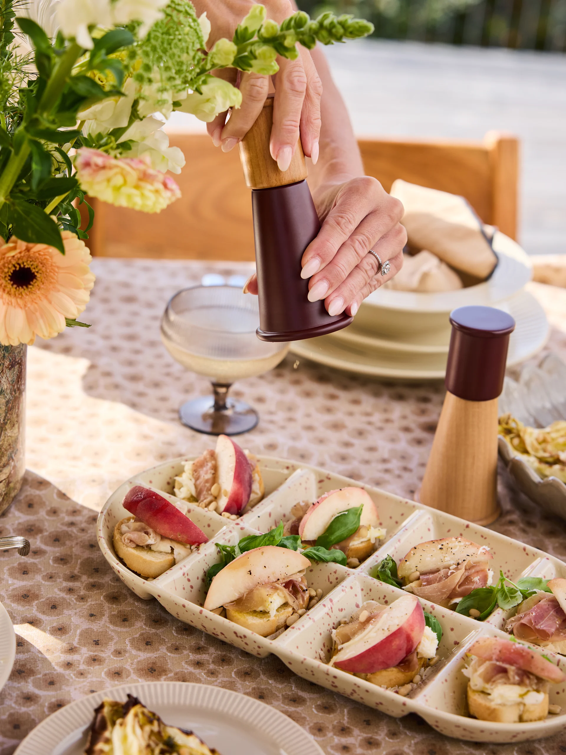 Handen malen peper op een crostini schaal met perziken, prosciutto, kaas, pijnboompitten, basilicum.