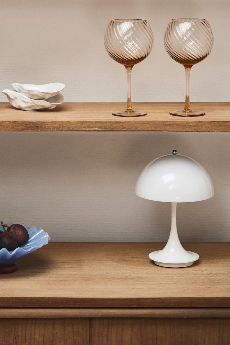 Verlevendig je huis met moderne lampen zoals de Panthella mini van Louis Poulsen, hier getoond in een houten vitrinekast met roze wijnglazen en een blauwe kom. 