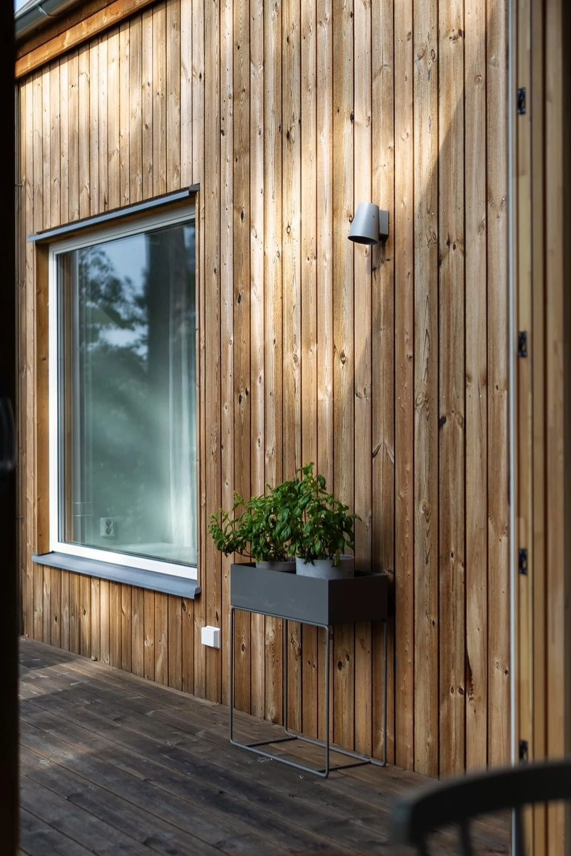 Hier zie je de zwarte metalen plantenbak van Ferm Living op het terras van een Zweeds houten huis staan.