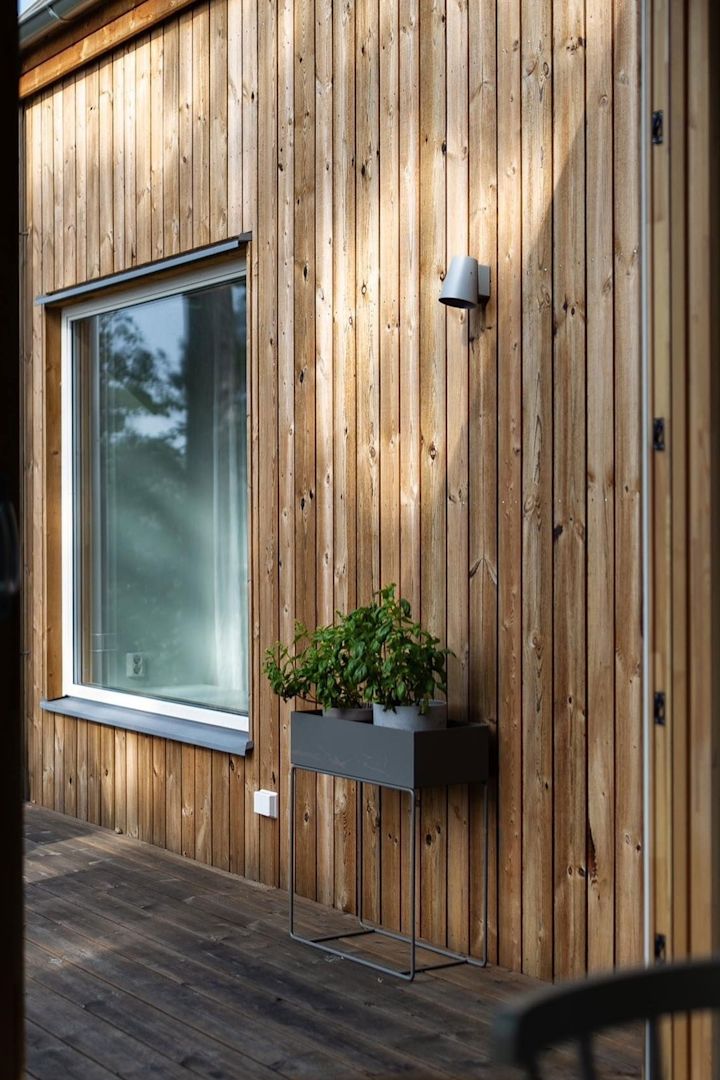 Hier zie je de zwarte metalen plantenbak van Ferm Living op het terras van een Zweeds houten huis staan.