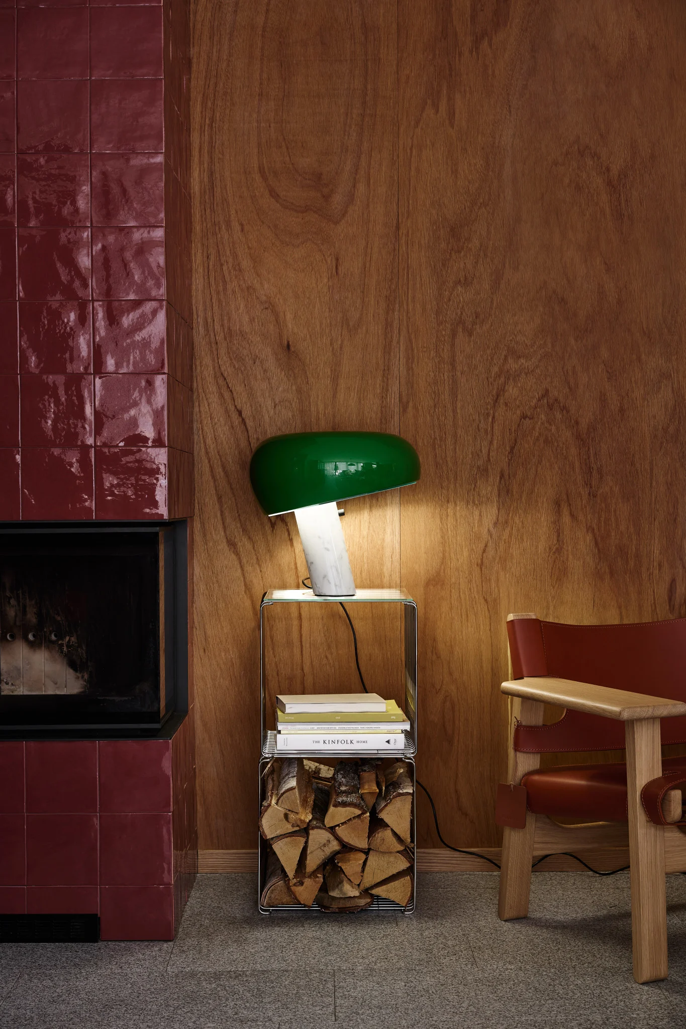 Een slaapkamer met crèmekleurig beddengoed met patroon, een geplooide lamp op een houten nachtkastje en een hoge spiegel, tegen bladbehang.