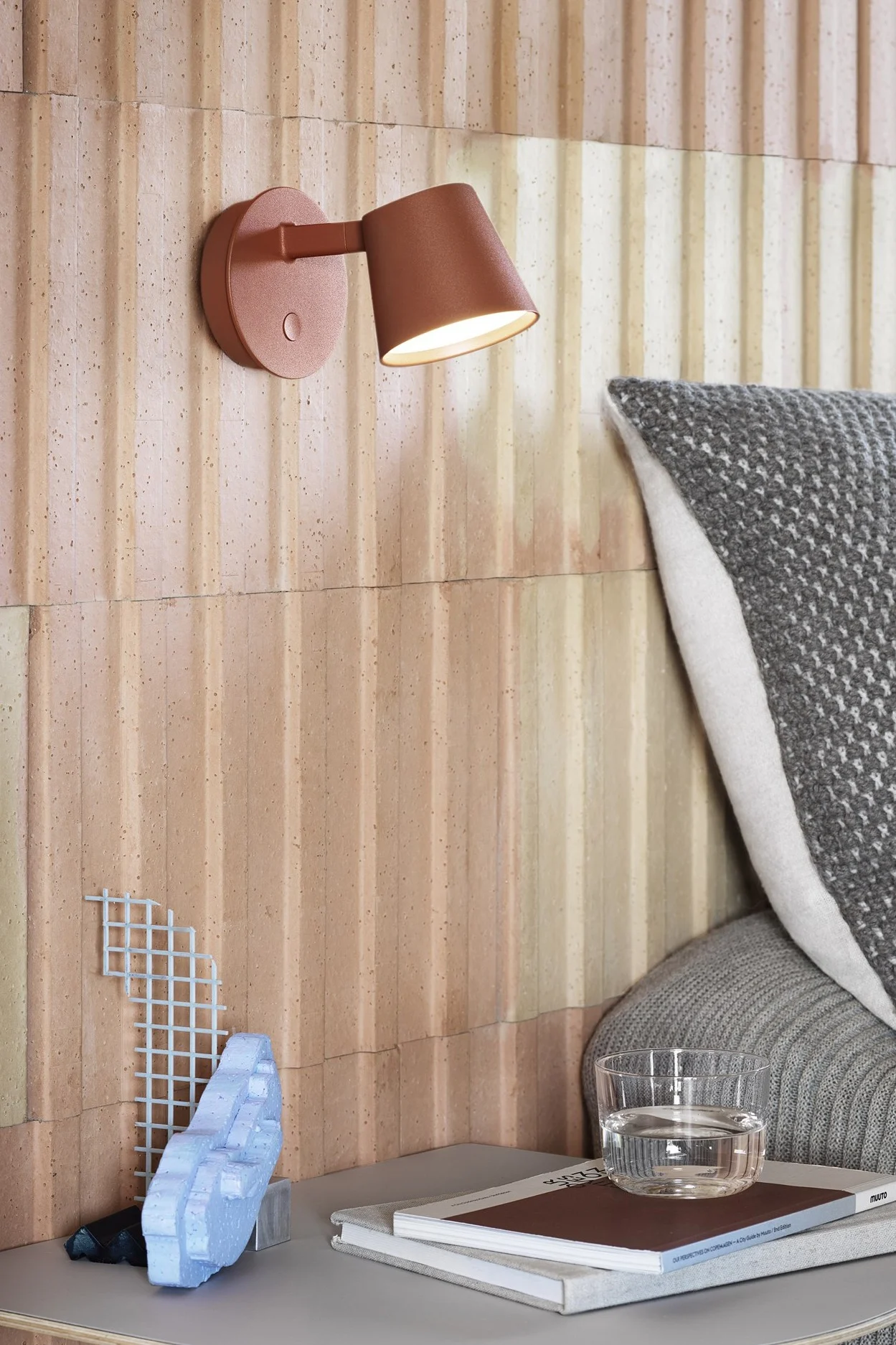 Moderne lampen die je huis verfraaien zijn onder andere stijlvolle wandlampen zoals de Tip wandlamp van Muuto, hier in het rood, die boven een nachtkastje is gemonteerd. 