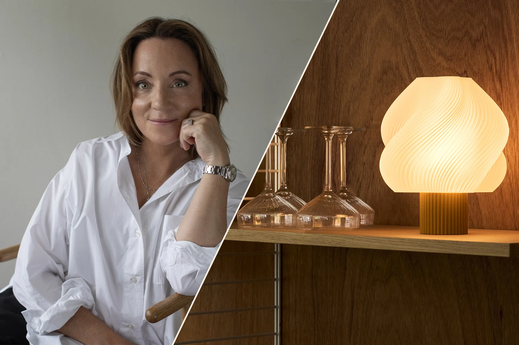 Lachende vrouw in een wit overhemd, kin op hand, draagt een horloge, in een warm, modern interieur met planken en een lamp.