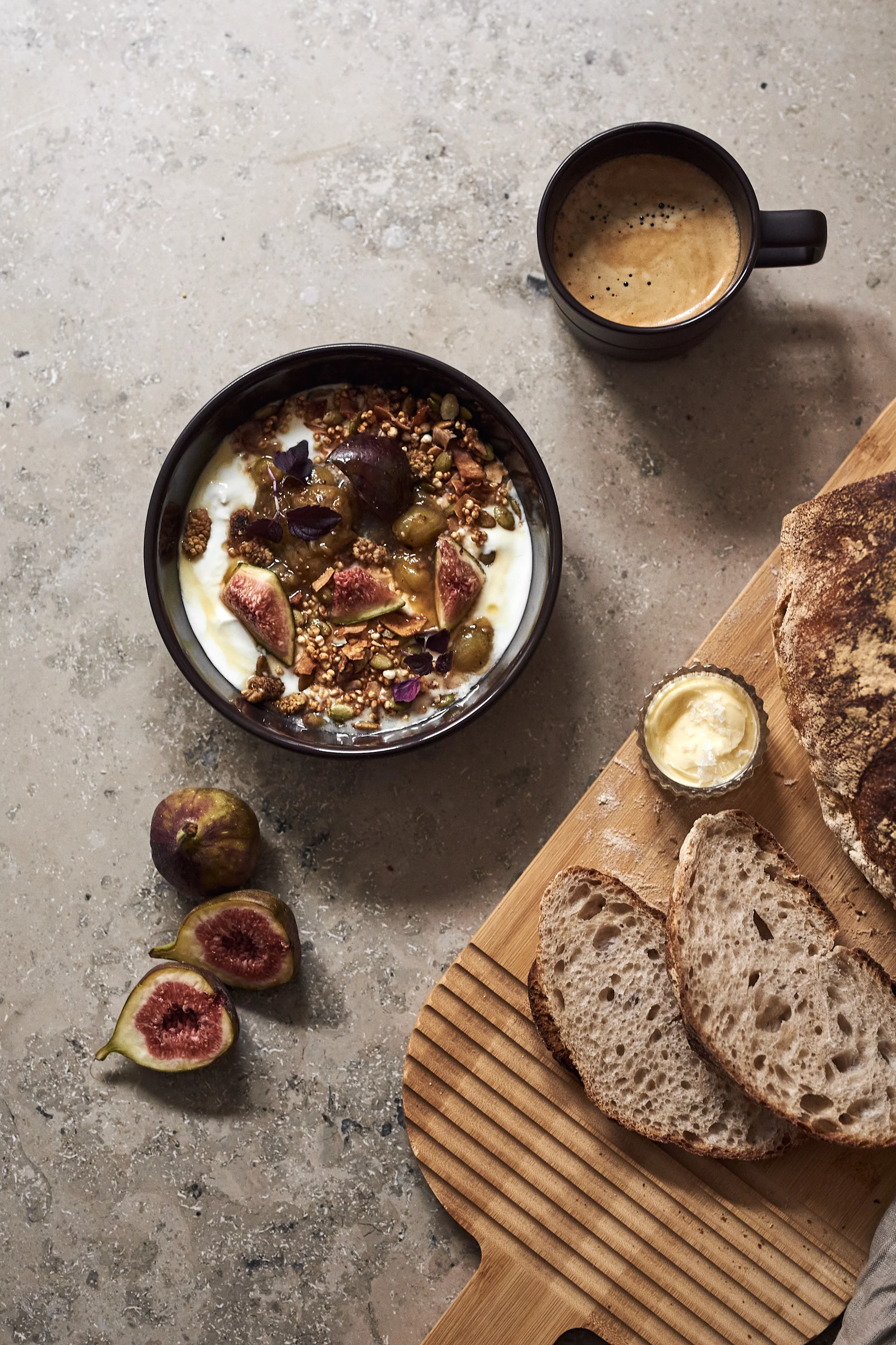 De bruine kom uit de Lines serie van NJRD met muesli, een kopje koffie en een houten plank met gesneden brood erop.