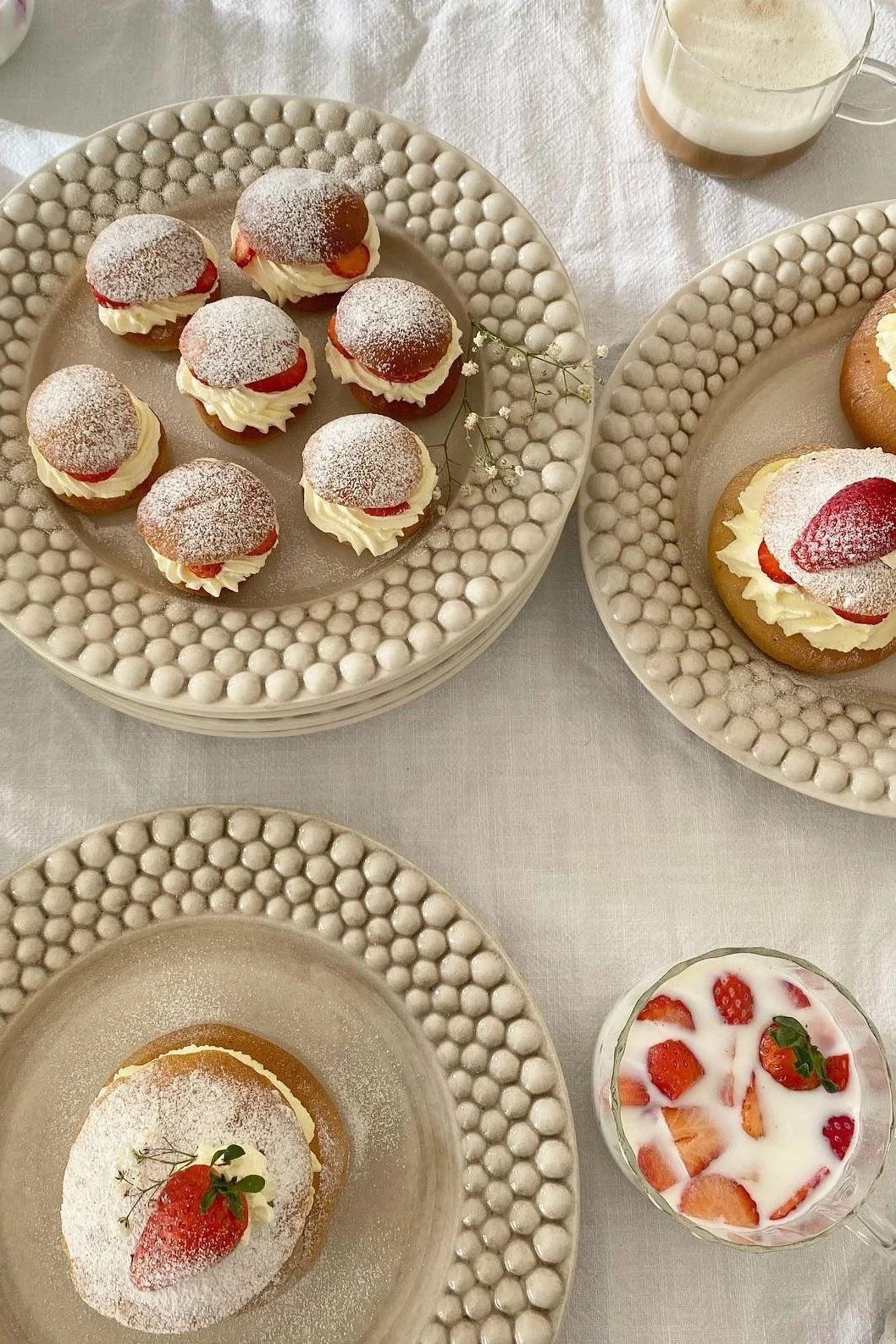 Roombollen met slagroom, aardbeien en poedersuiker op gestructureerde borden, met drankjes.