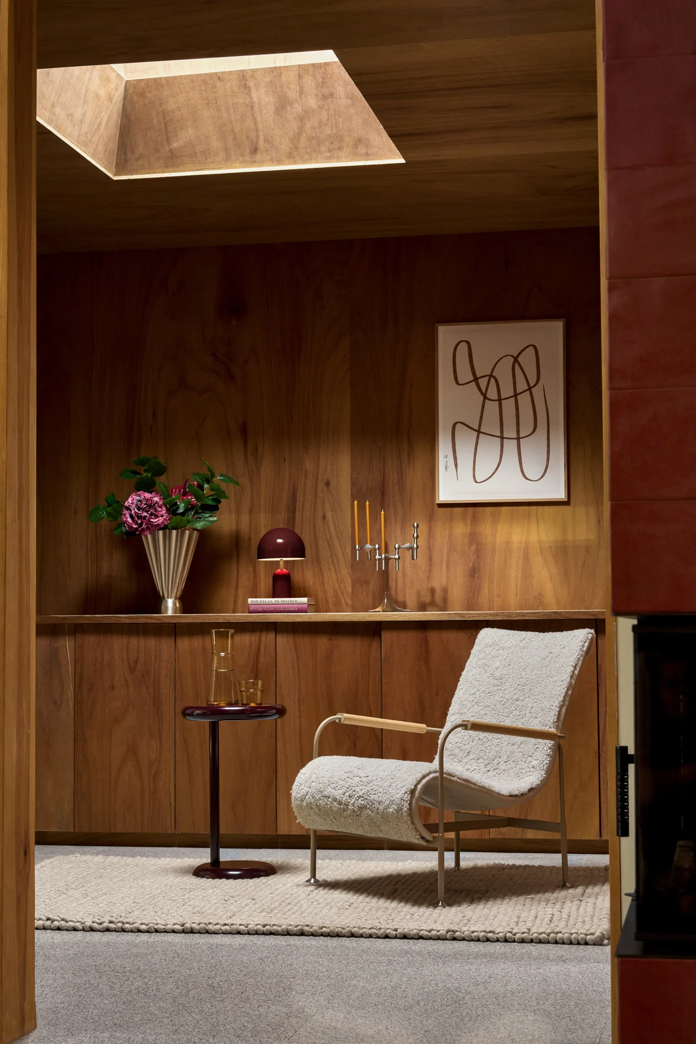 Gezellige kamer met houten wanden, crèmekleurige bouclé fauteuil, bijzettafel, bloemen en abstracte kunst.