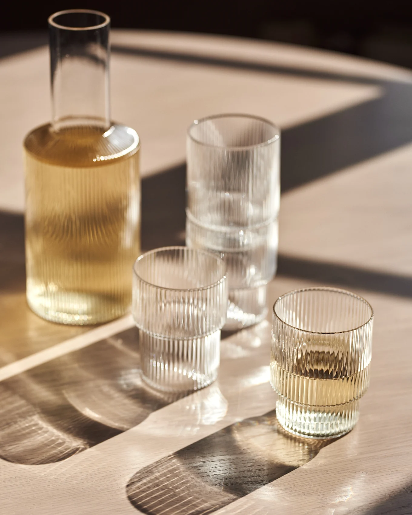 Glazen karaf en geribbelde glazen op een houten tafel met zonlicht.