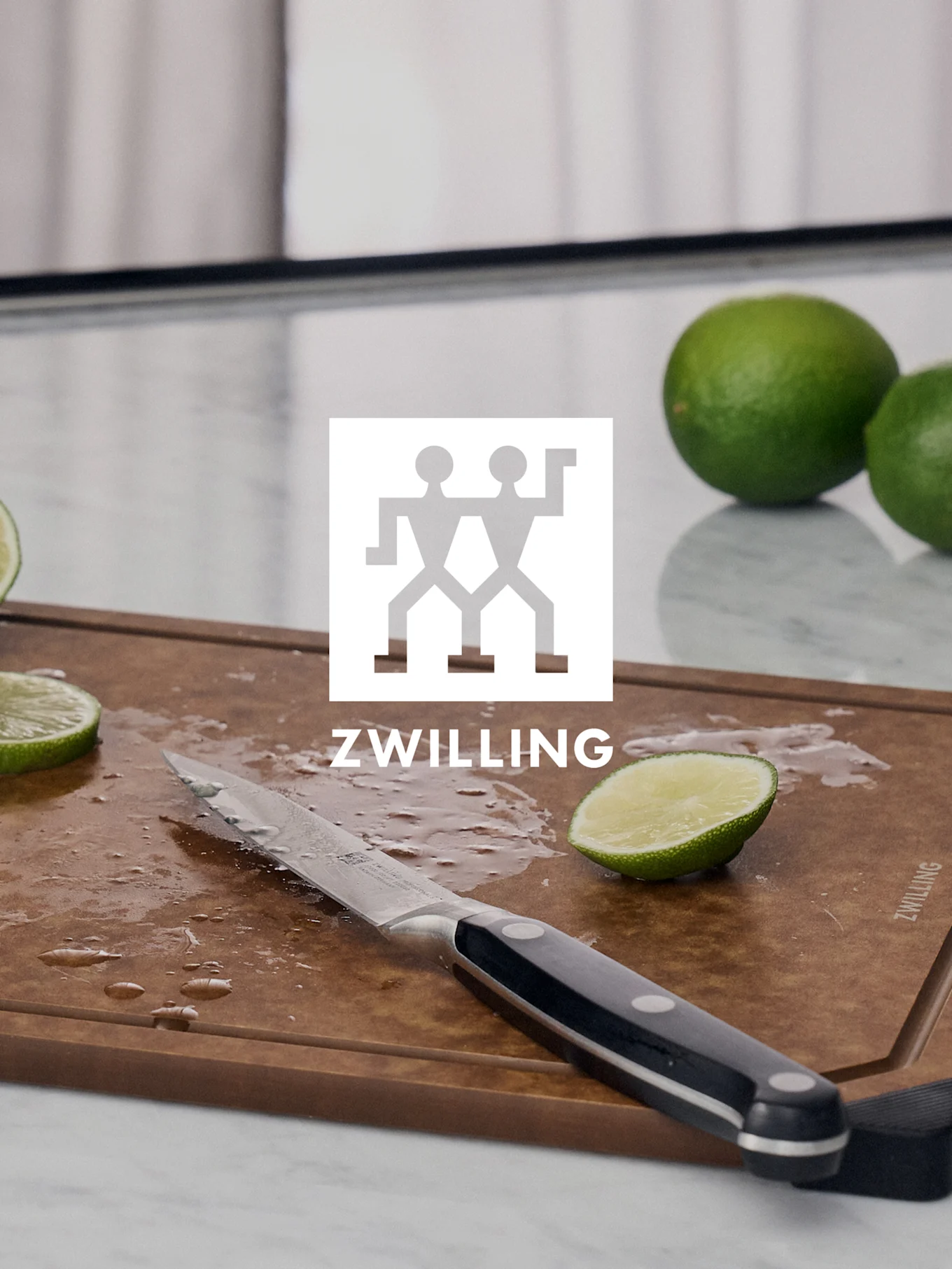 ZWILLING-logo boven een snijplank met een mes, gesneden limoen en hele limoenen.