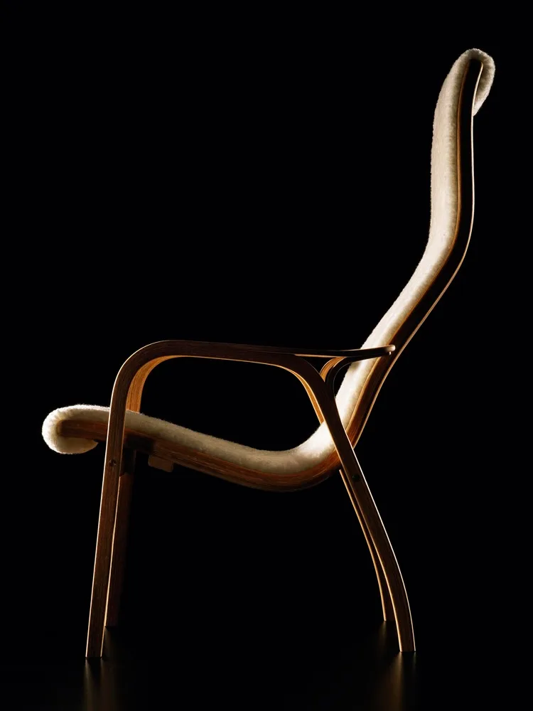 Een elegante loungestoel met een gebogen licht houten frame en crèmekleurige harige bekleding, tegen een zwarte achtergrond.
