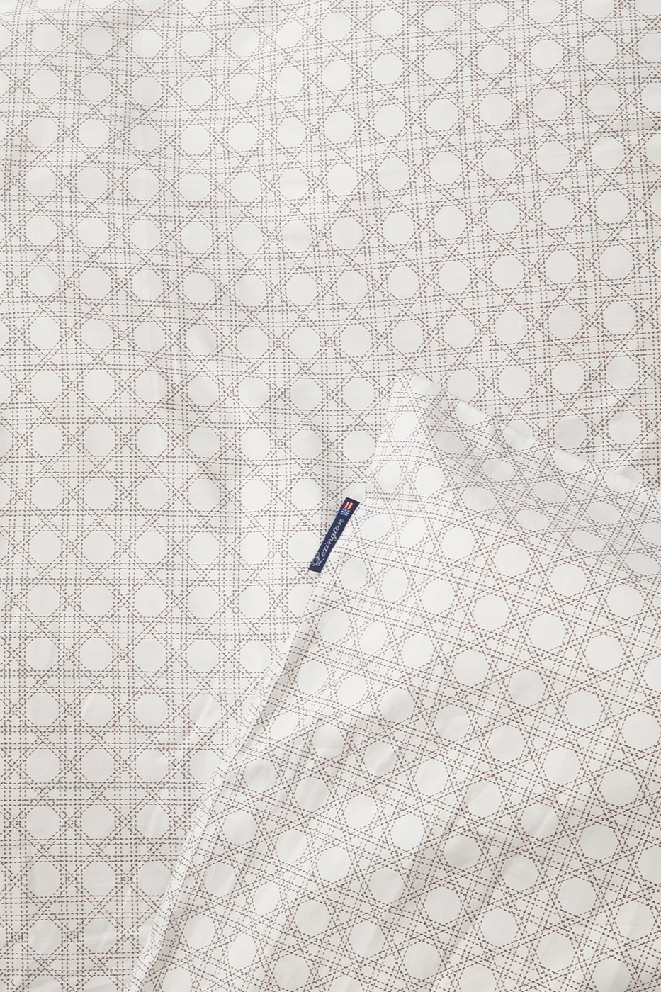 Witte stof met lichtbruin rotanpatroon en een blauw Lexington-label.