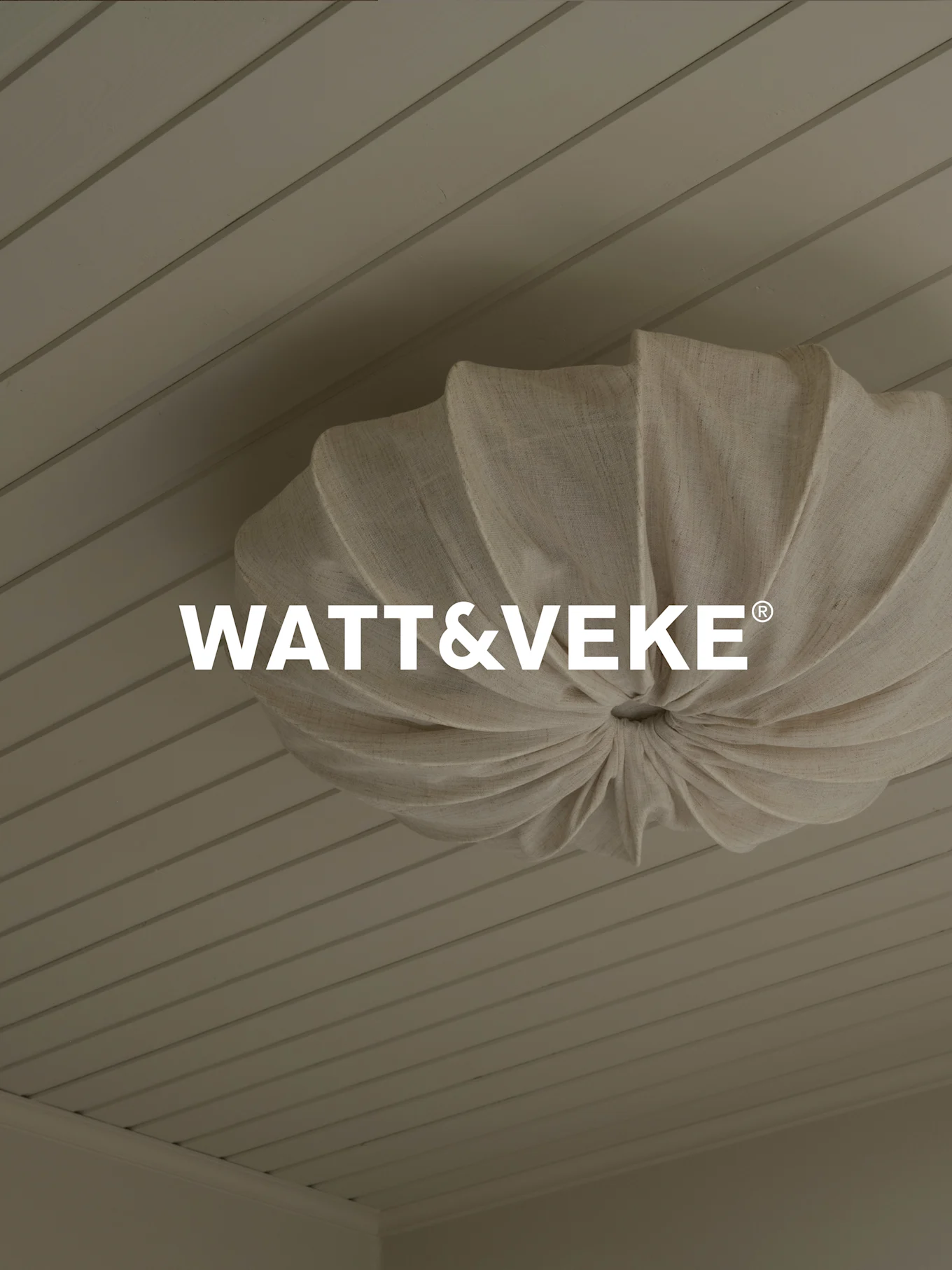 WATT&VEKE®-logo boven een geplooide plafondlamp van natuurlijke stof aan een licht houten plafond.