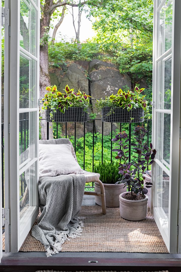 Een klein, gezellig ingericht balkon met een lounge stoel en verschillende planten, onder andere in de Korbo-balkonmand.