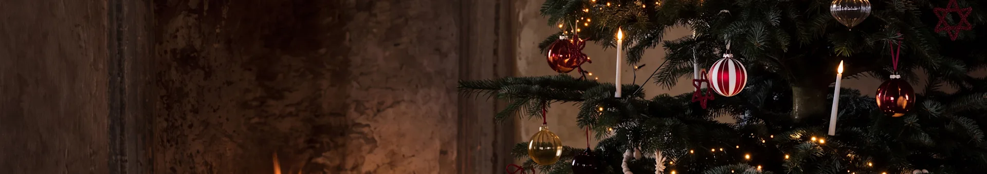 Een feestelijke kerstboom met versieringen en een brandende kaars naast een warme open haard met brandend hout.
