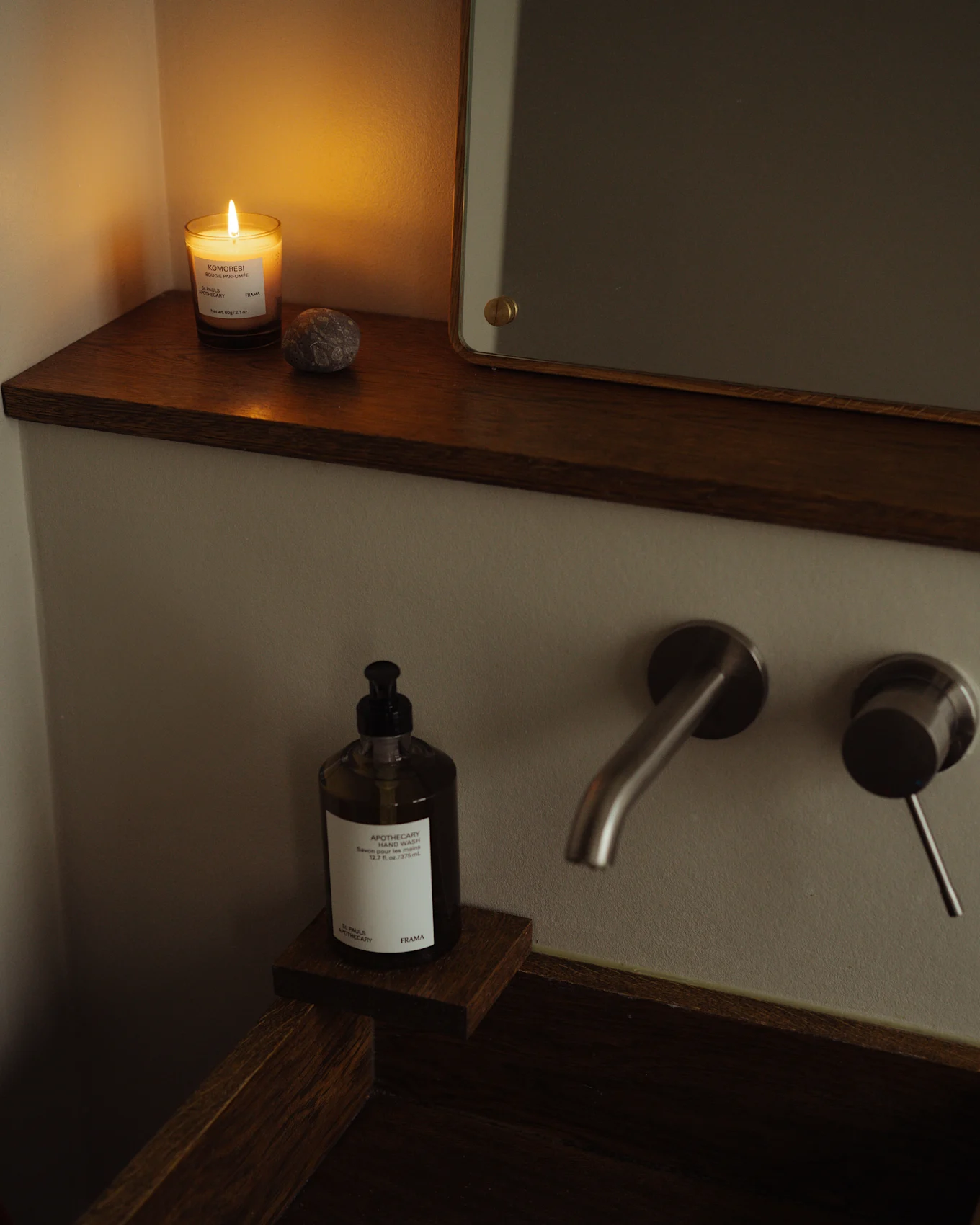 Gezellige badkamer met brandende kaars, handzeepfles en geborstelde metalen kraan bij een donkerhouten wastafel.