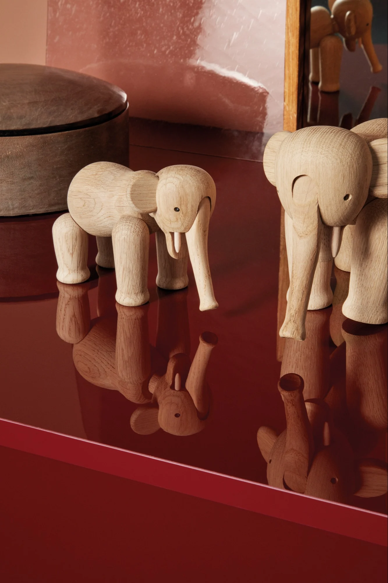 Twee lichte houten olifantenbeeldjes staan op een reflecterend rood oppervlak.