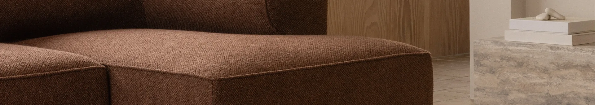 Close-up van een bruine getextureerde bank, met houten muur en decoratieve objecten op beton.