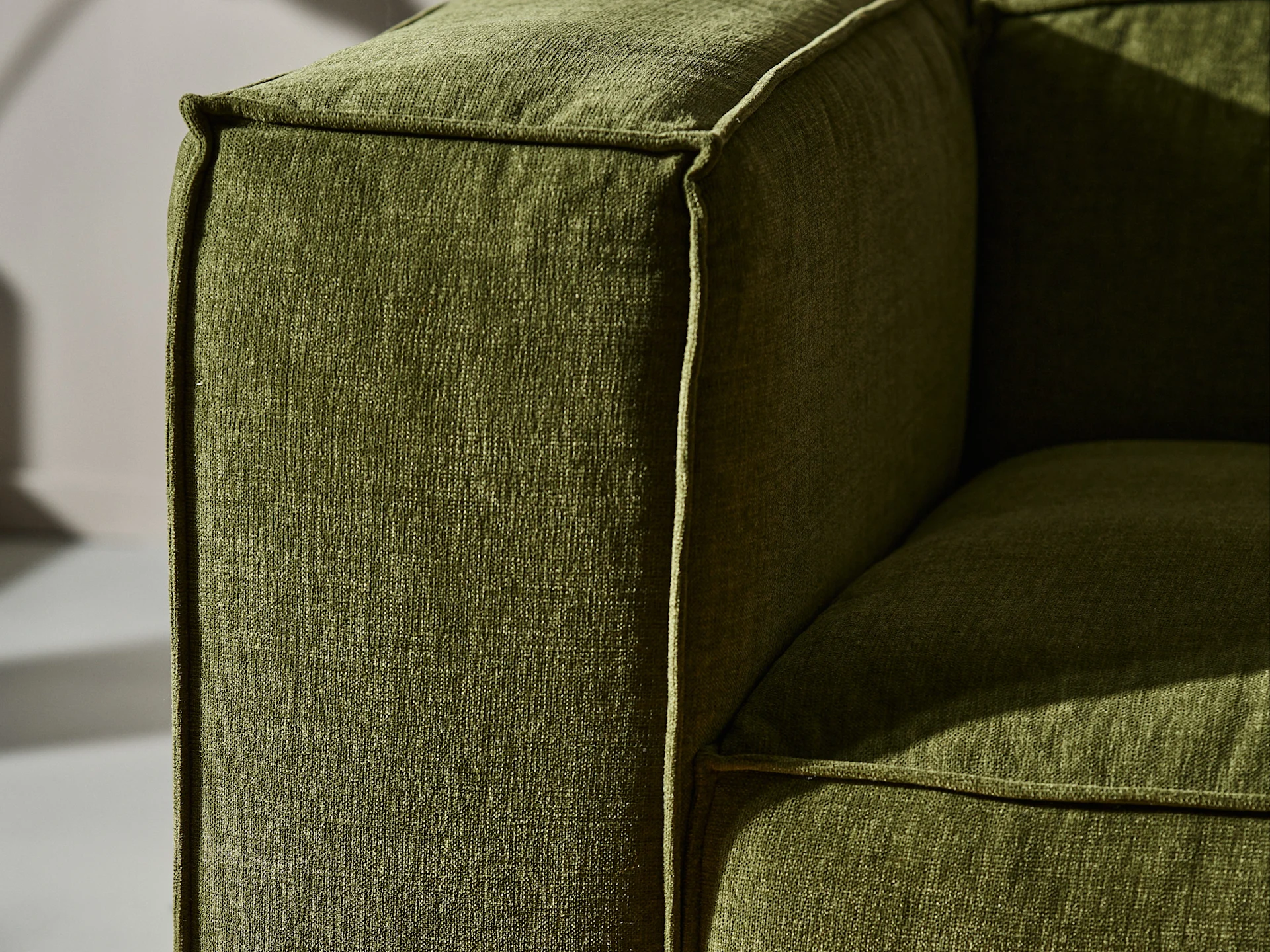Close-up van een groene stoffen bankleuning met zichtbare textuur en biezen.