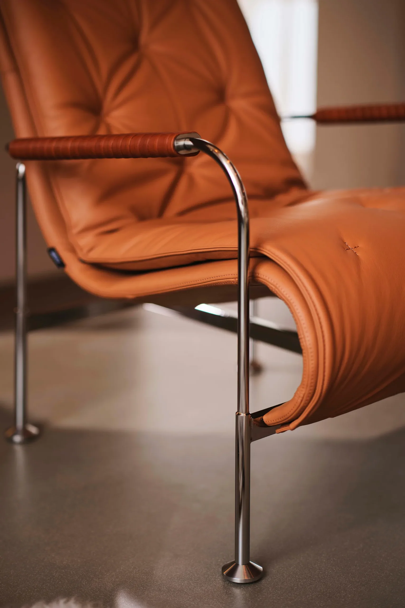 Cognackleurige leren fauteuil met chromen frame en omwikkelde armleuningen.