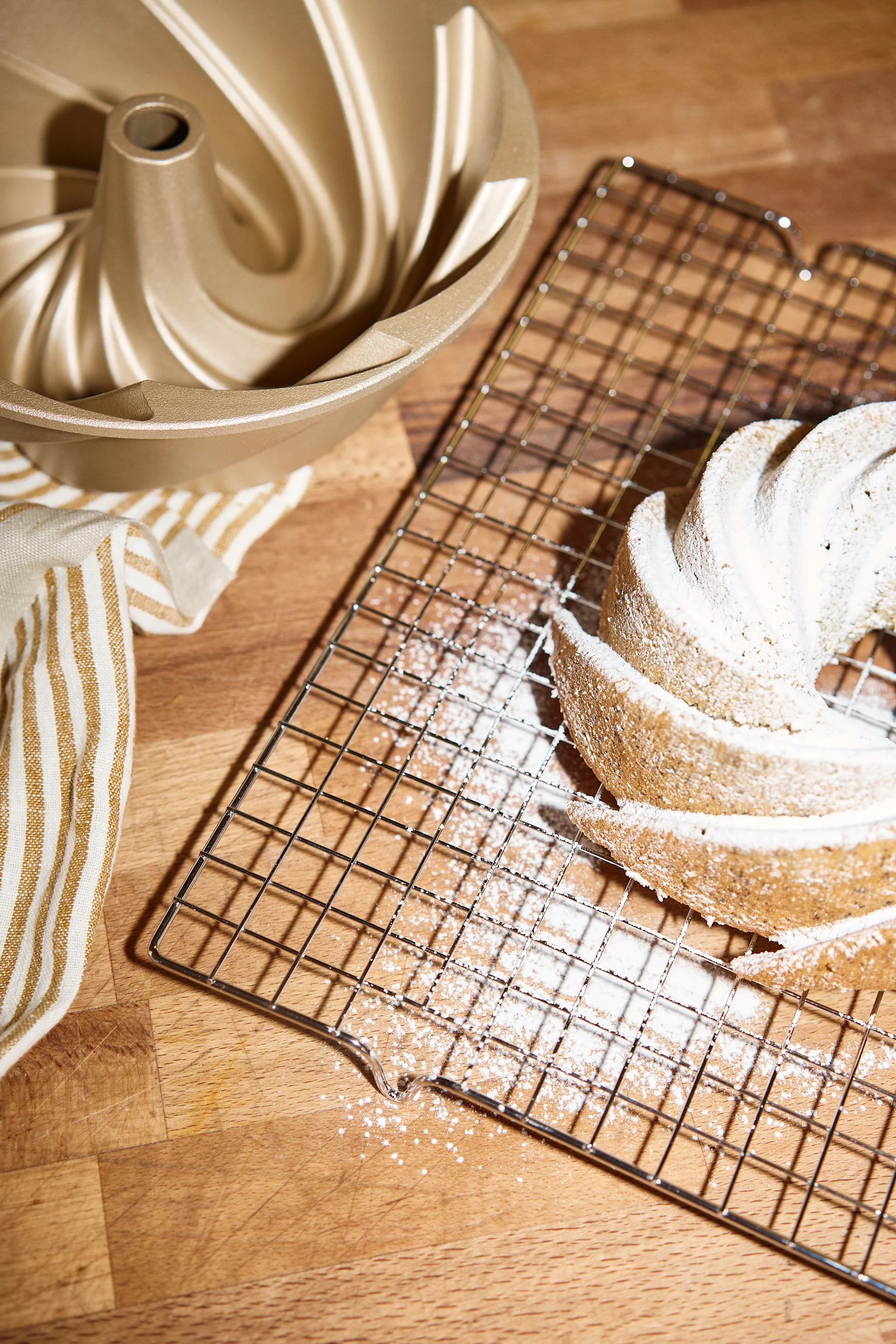 Een gouden tulbandvorm, een gestreepte handdoek en een tulbandcake bestrooid met poedersuiker op een koelrek.