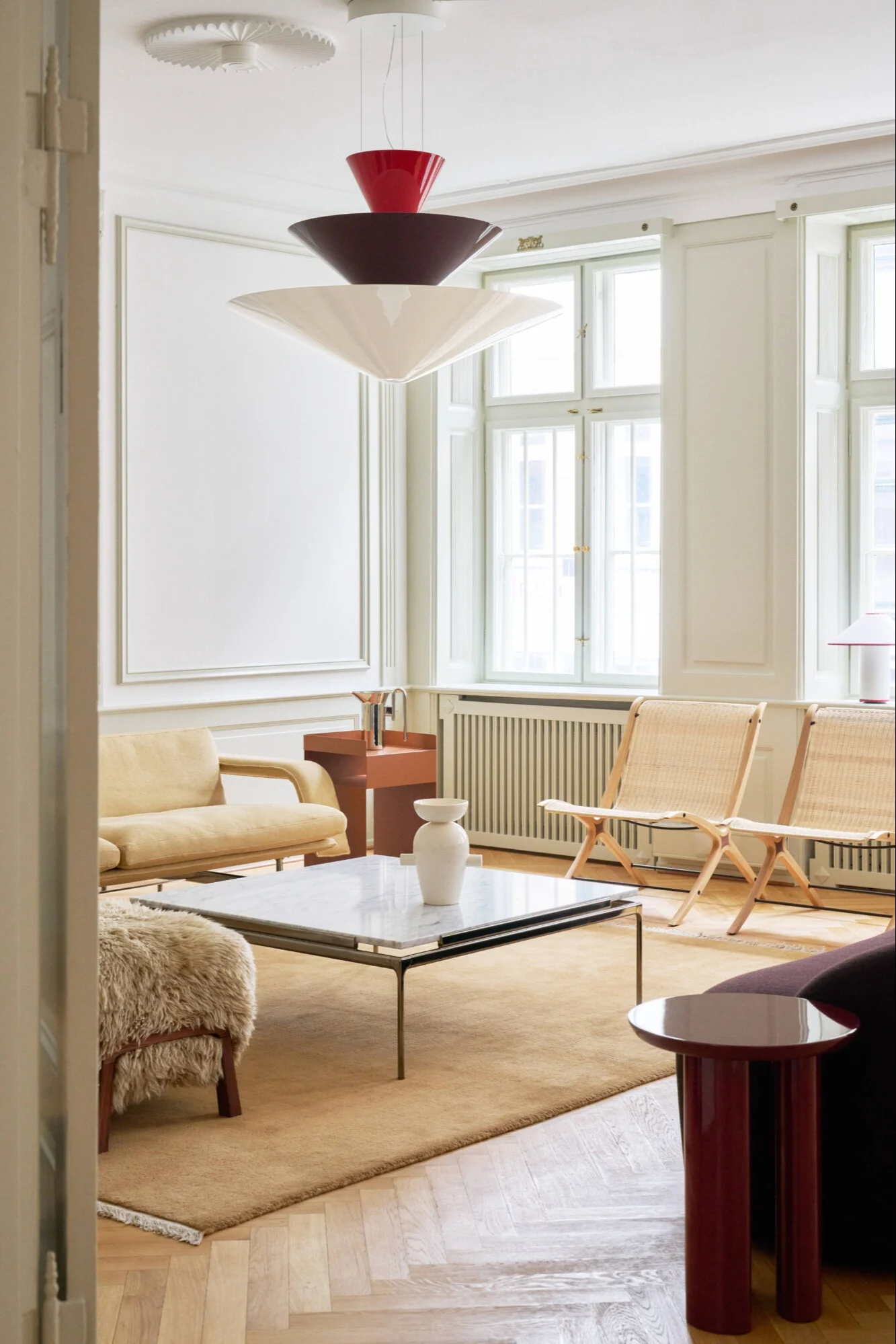 Een moderne woonkamer met een gelaagde hanglamp, lichtgele bank, rotan stoelen en marmeren salontafel.