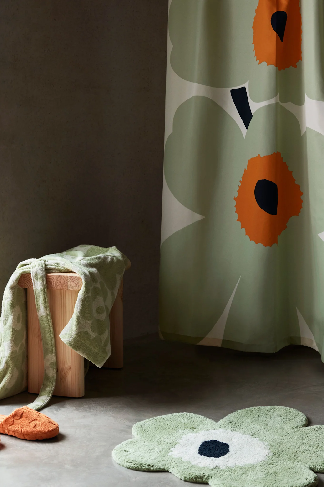 Badkamerinrichting met groen bloemen douchegordijn, badmat, handdoek op kruk en oranje slipper.