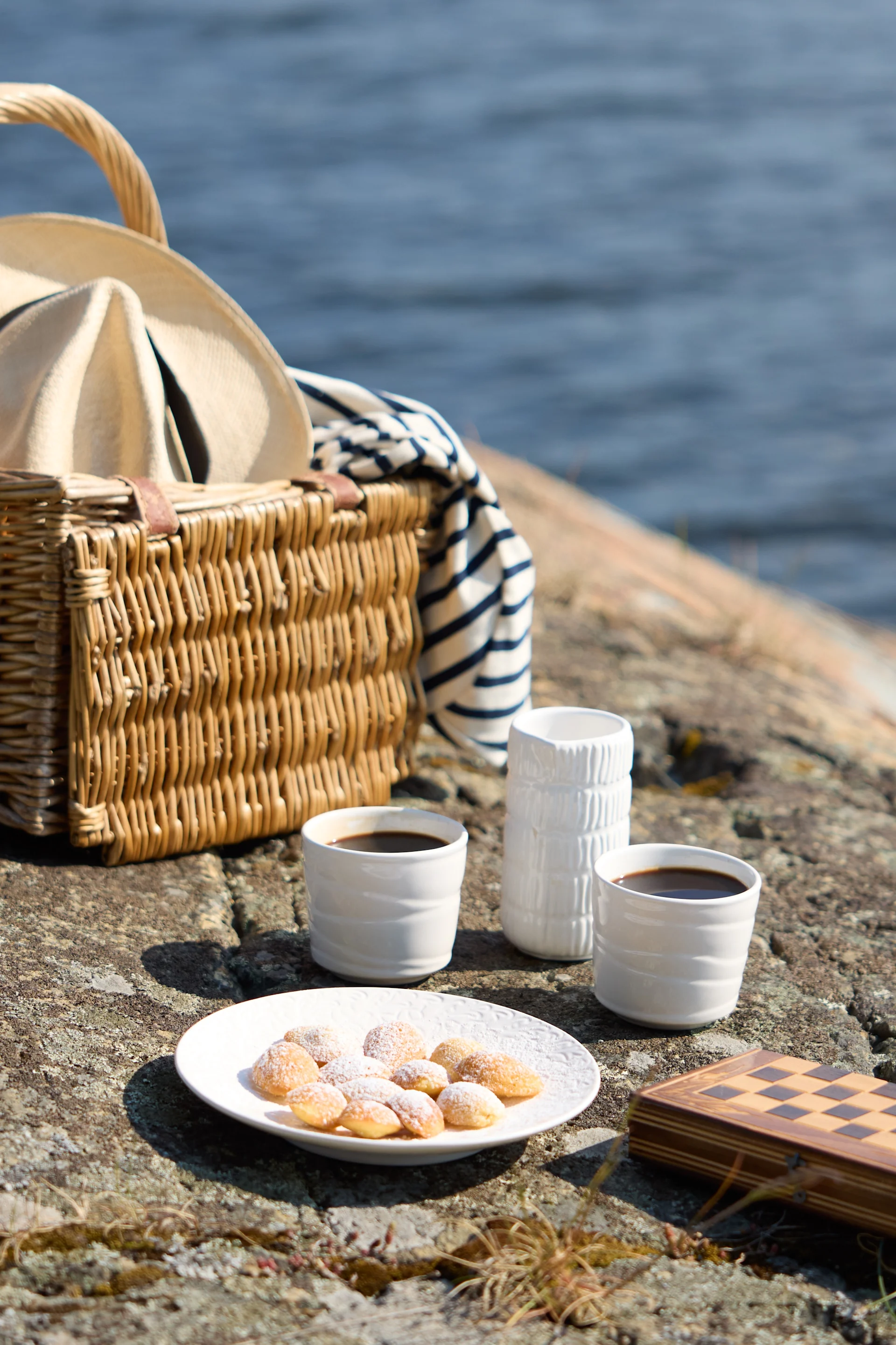 Een picknick op rotsachtig terrein bij het water, met koffie, gebak en een schaakspel.