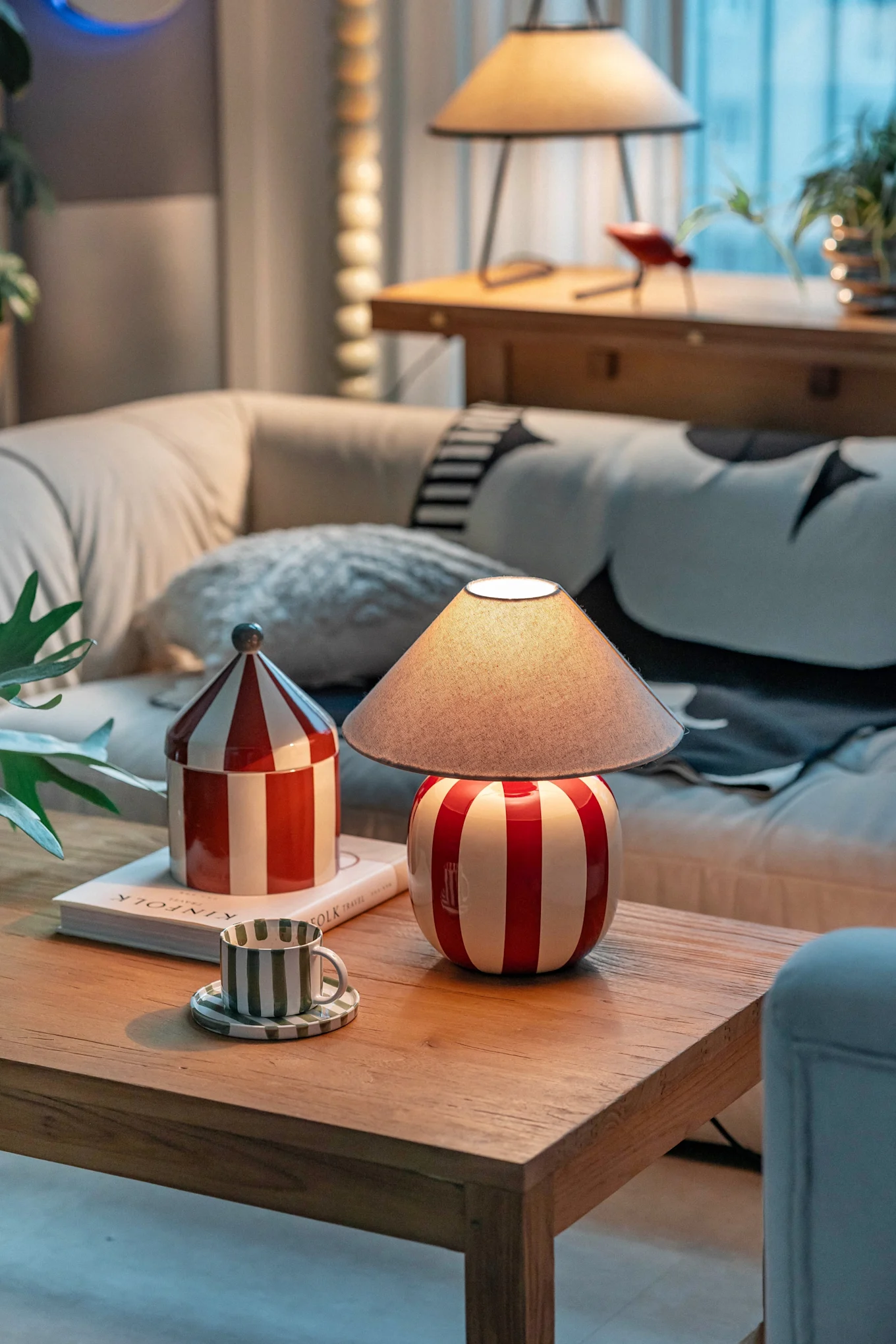 Een gezellige woonkamer met een rood-wit gestreepte lamp, bijpassende bus en een groen gestreepte kop op een houten salontafel.