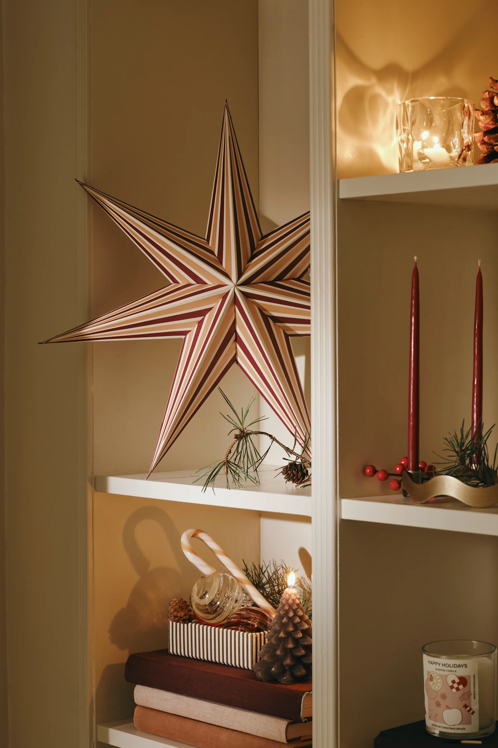 Twee grote rode papieren sterren hangen in een moderne woonkamer met een lichte bank en doorschijnende gordijnen.