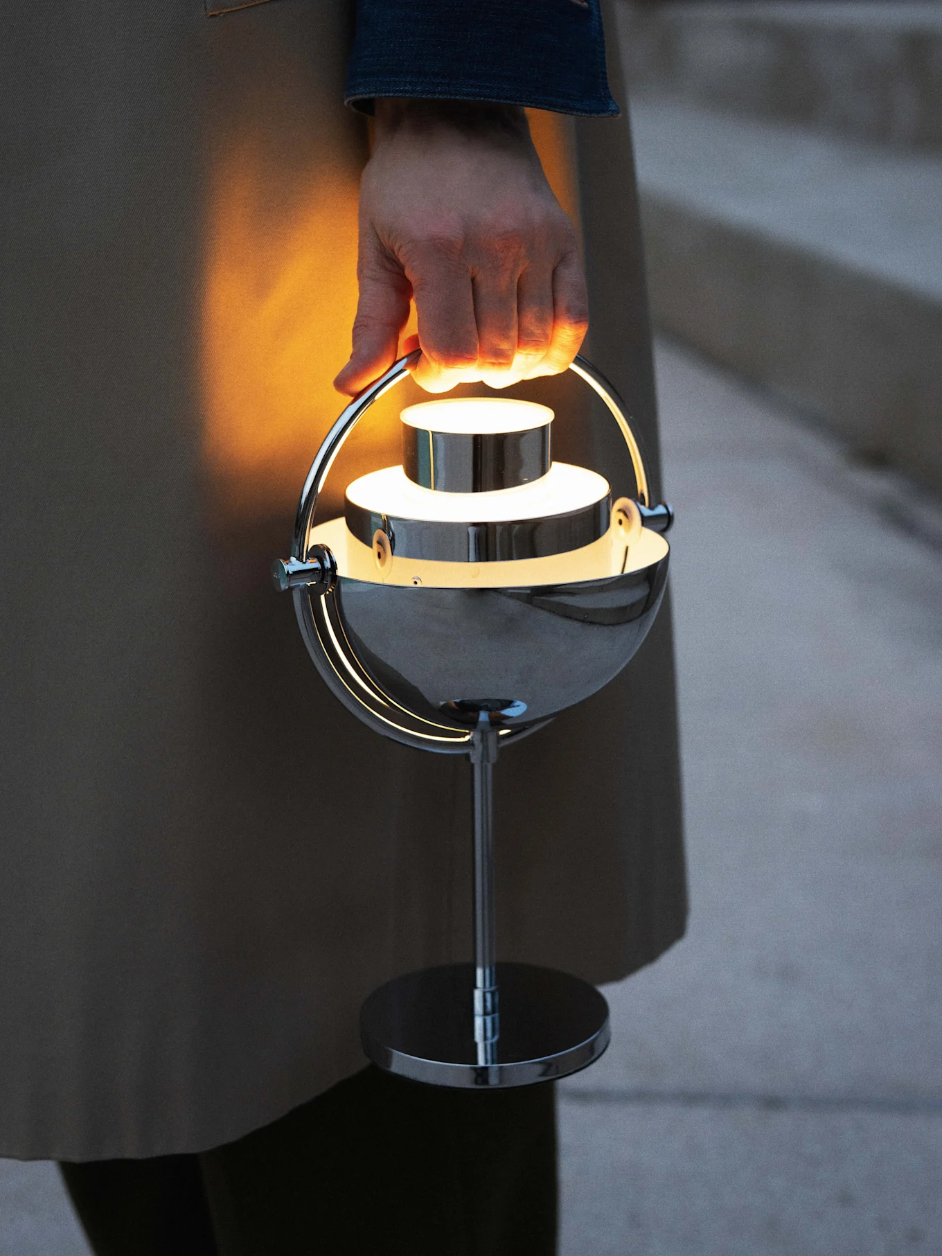 Hand houdt een gloeiende, moderne chromen draagbare lamp vast.