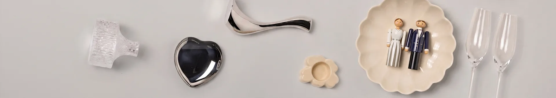 Decoratieve items: glazen knop, zilveren hart, gebogen handgreep, bloemen schaal, bruidspaar figuren, champagneglazen.