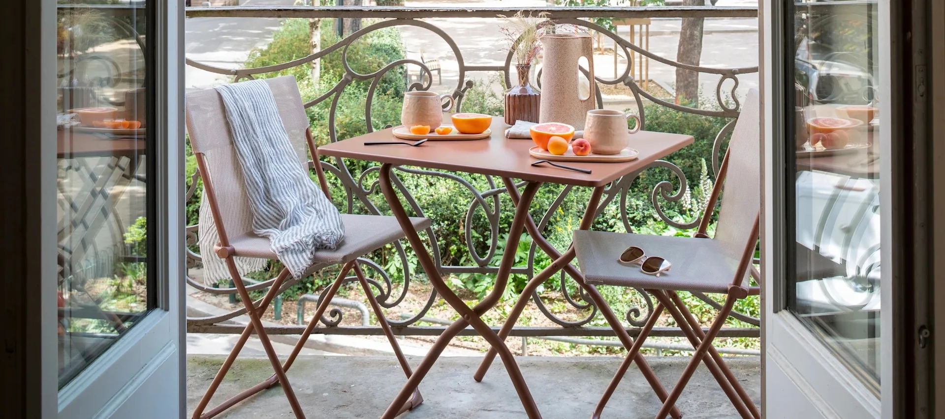Een klein balkon met terracotta gekleurde klapstoelen en tafels.