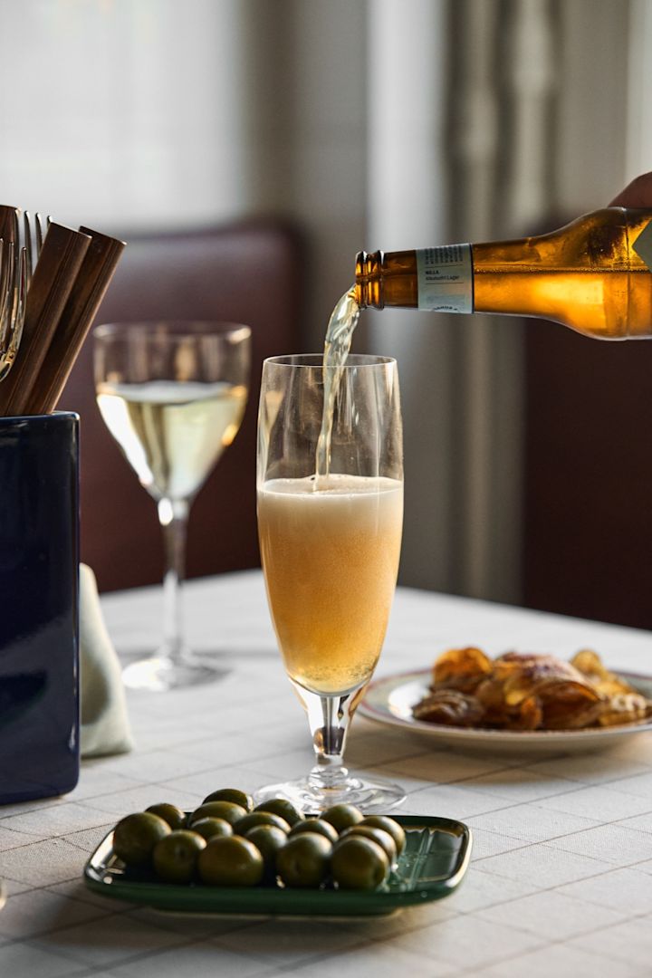 Ontdek welk bierglas bij welk bier hoort: Hier zie je hoe een biertje wordt ingeschonken in het Chateau bierglas van Kosta Boda, met een bordje olijven ernaast.