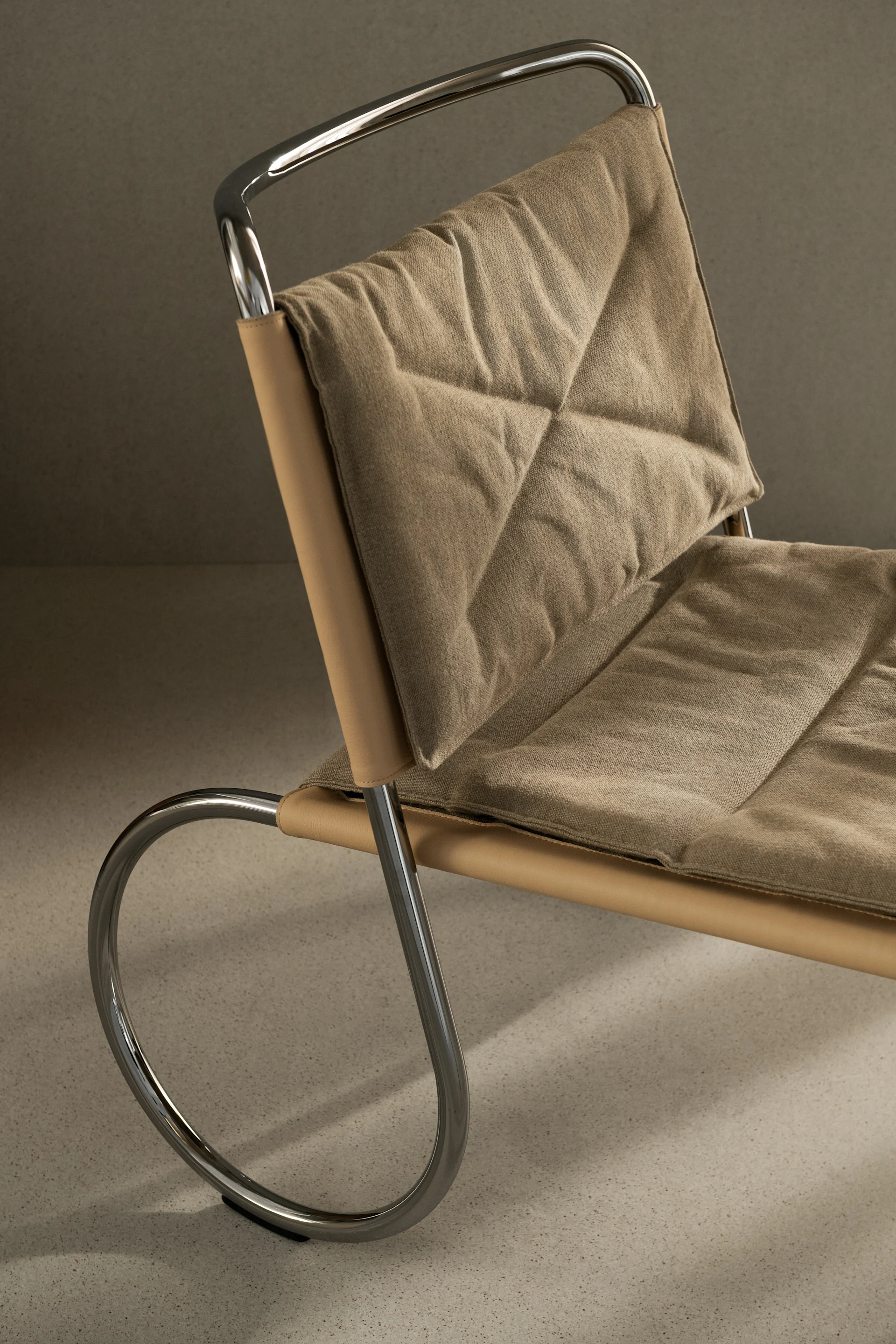 Close-up van een moderne stoel met een gepolijst chromen frame, een lichtbruine leren zitting en gewatteerde beige stoffen kussens.